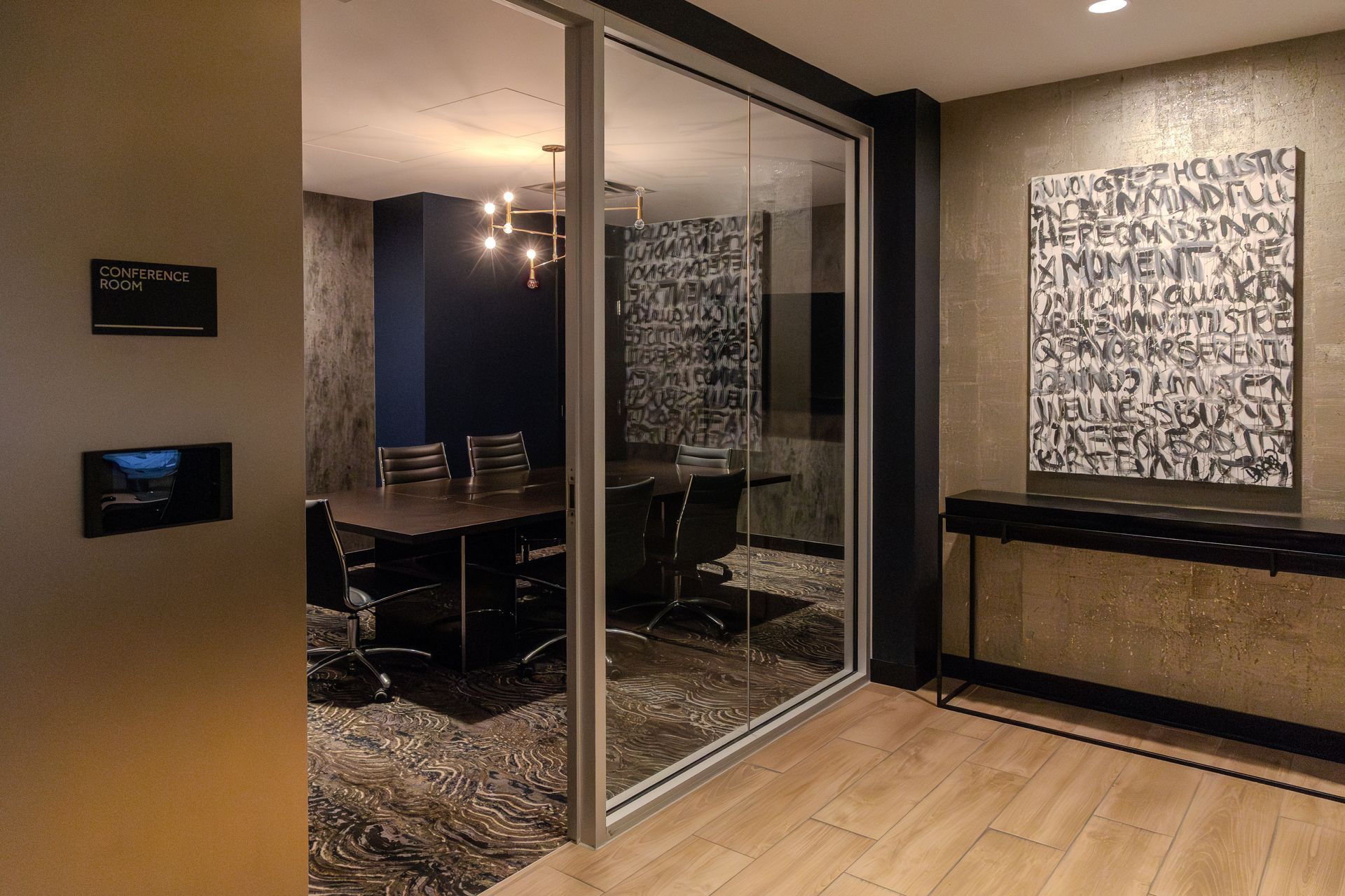 Modern office conference room with glass wall, dark furniture, and abstract art.