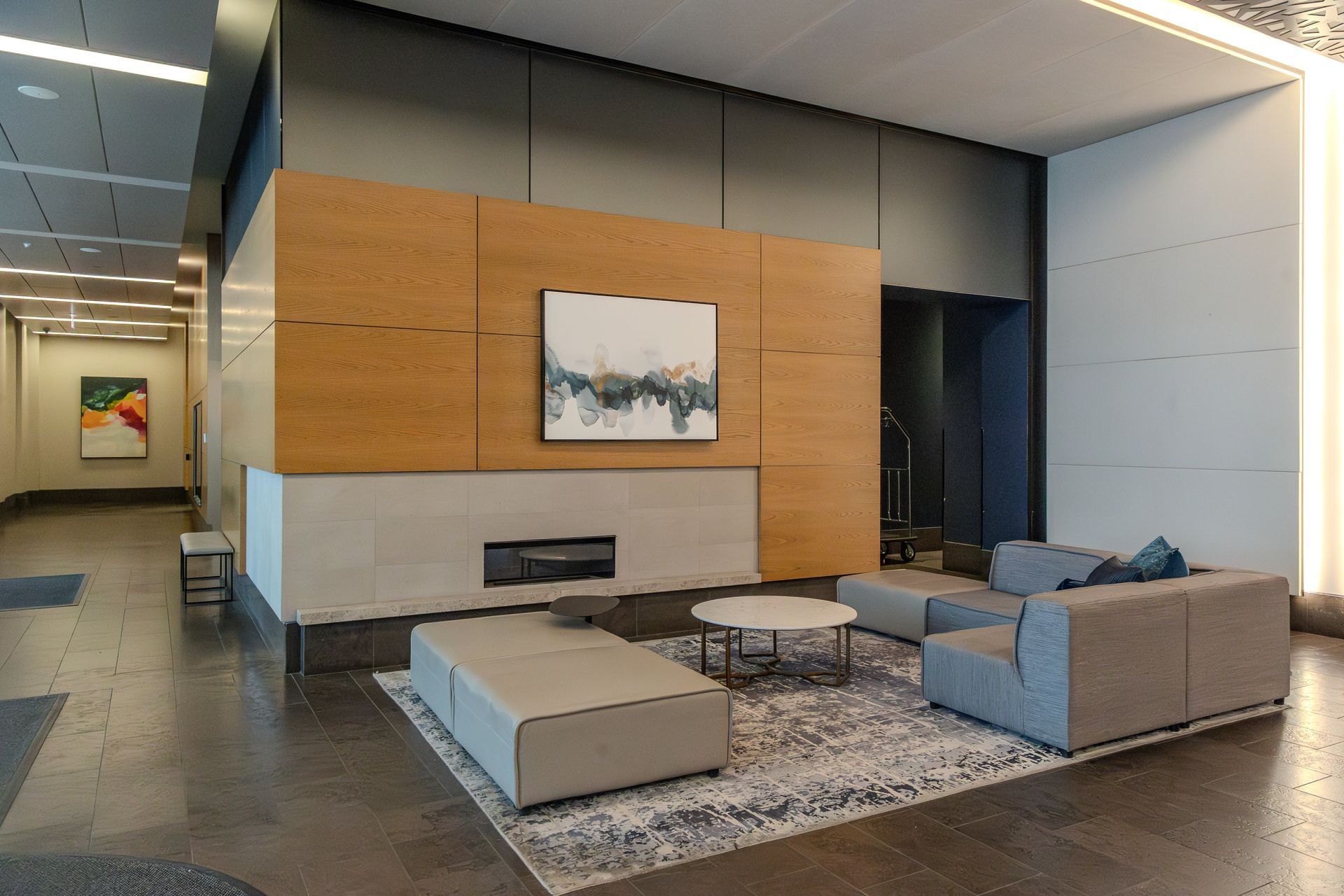 Modern lobby with a seating area. Light wood paneling, artwork, couches, and a rug.