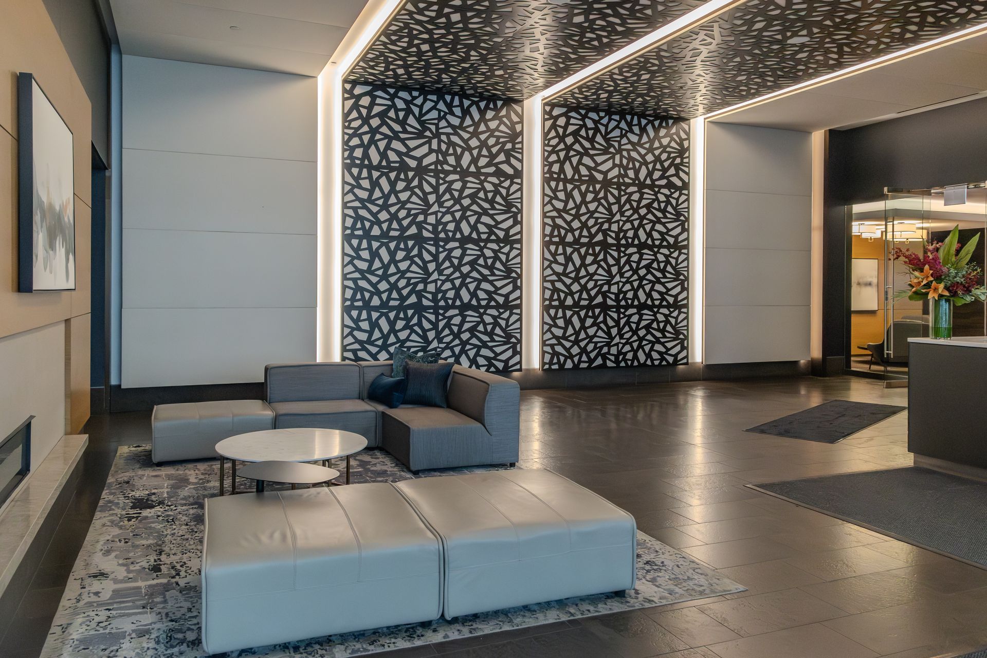 Modern lobby with gray couches, patterned wall, and decorative lighting.