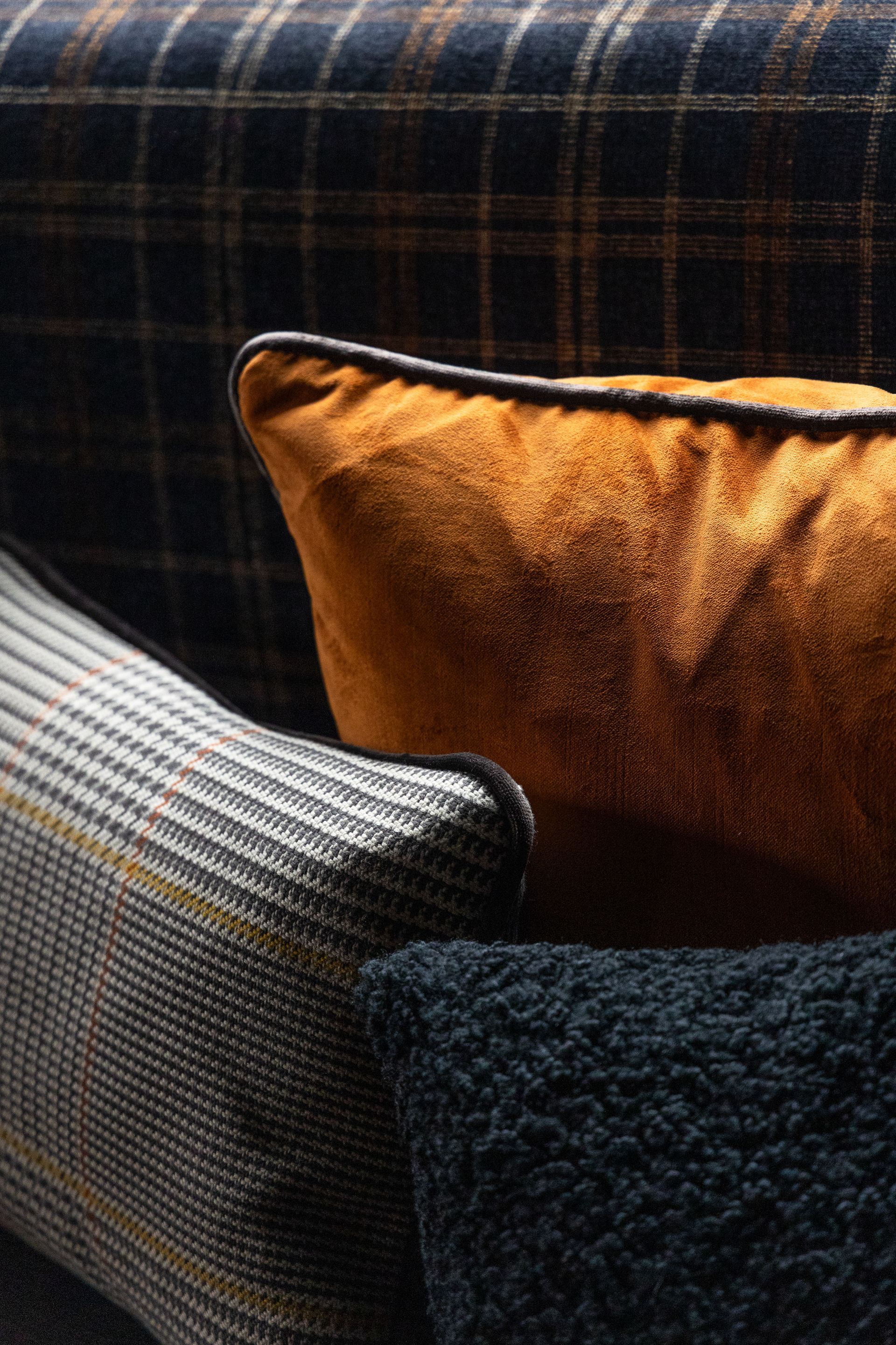 Couch with patterned plaid back and multiple pillows: gold, gray plaid, and dark blue textures.