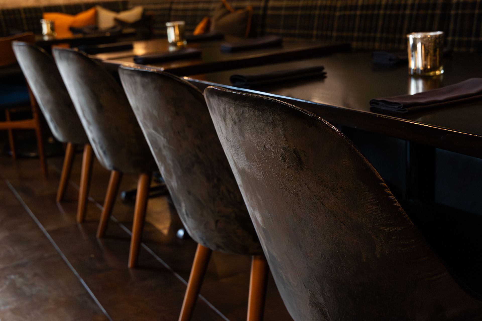 Row of gray velvet chairs at a dark wood table in a restaurant setting.