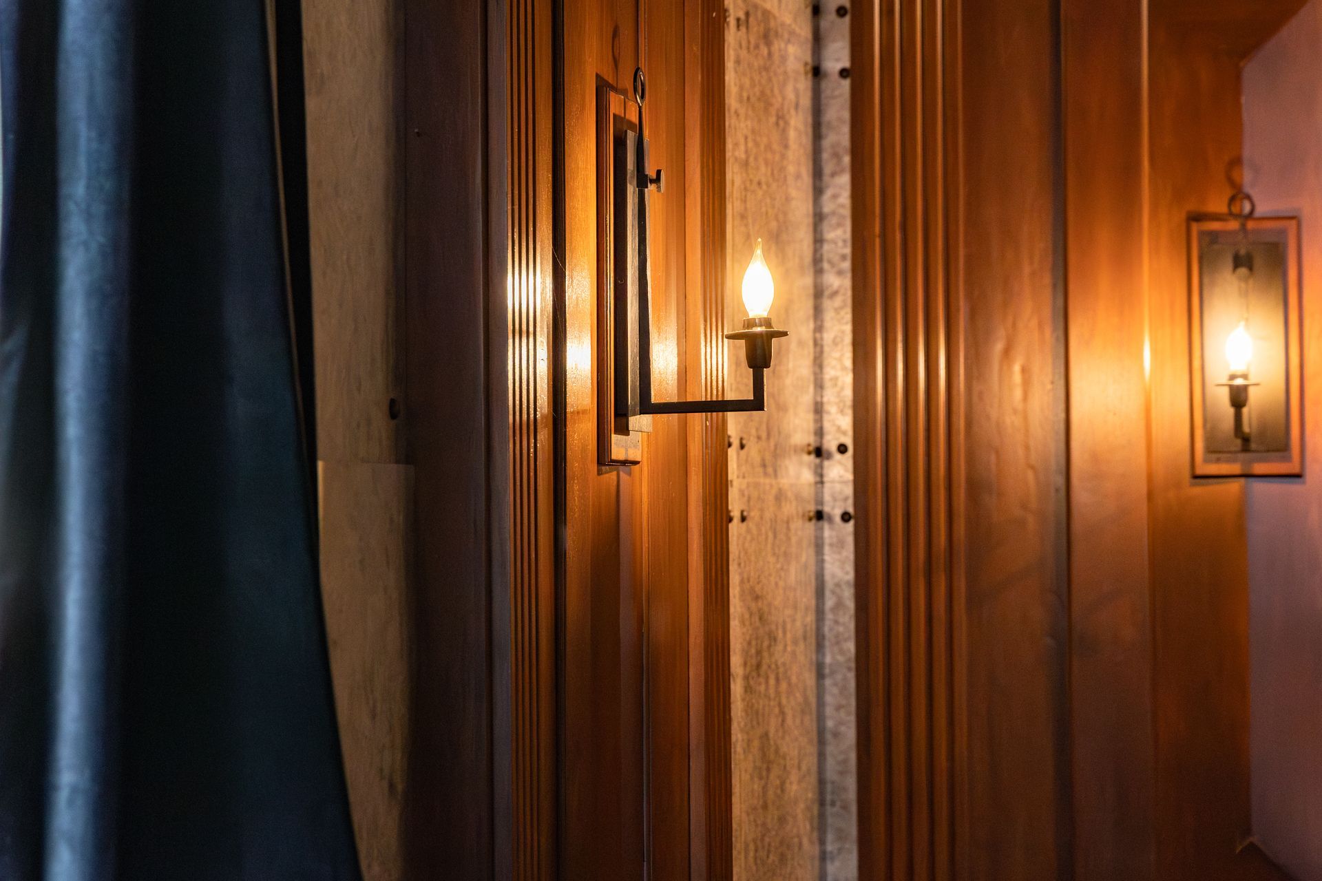Warm wooden hallway with lit wall sconces and a dark curtain on the left