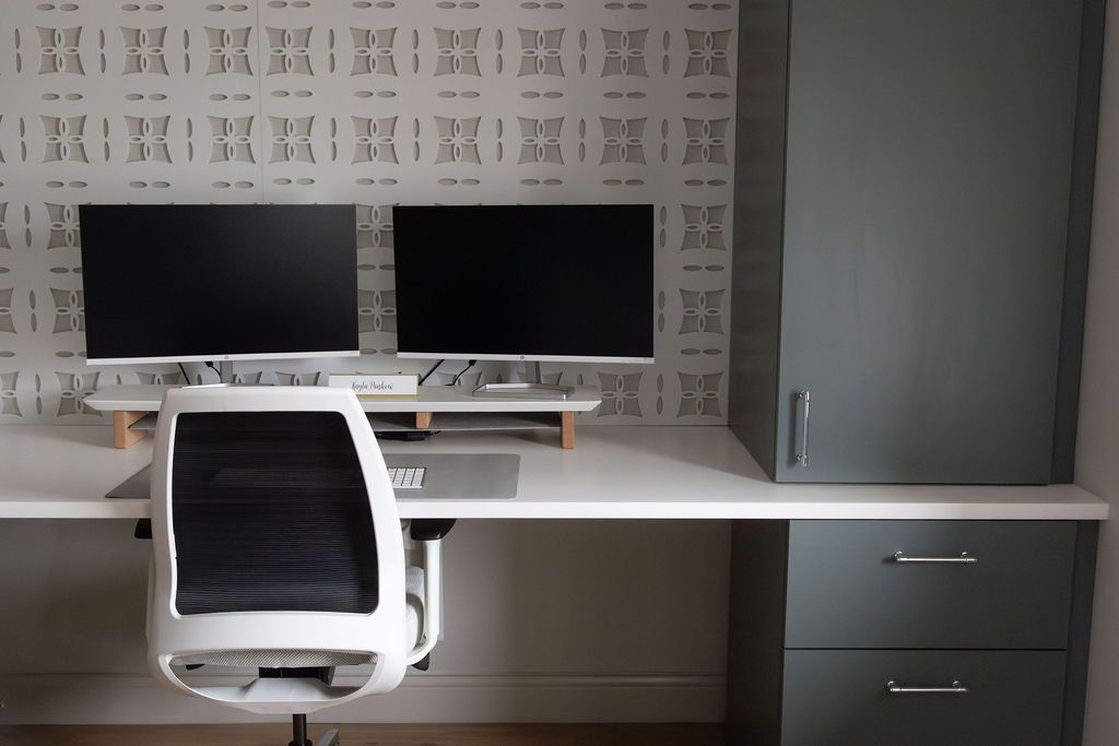 Home office with white desk, dual monitors, gray cabinetry, and white ergonomic chair.