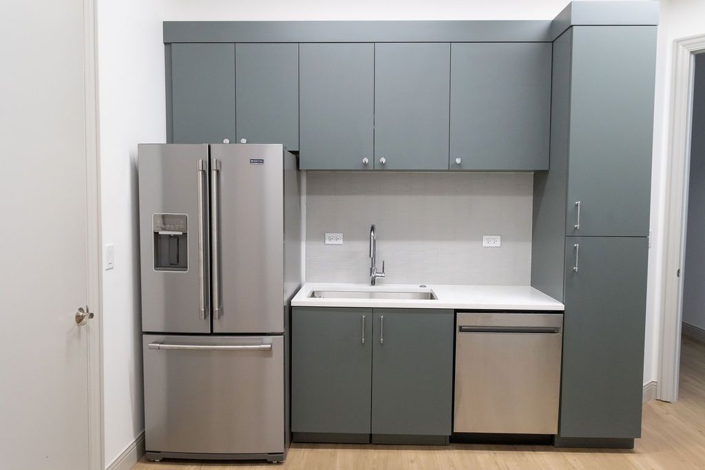 Modern kitchen with gray cabinets, stainless steel appliances, and a white countertop.