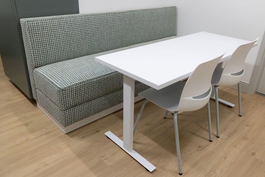 A booth with patterned upholstery and a white table with two white chairs in a room with light wooden floors.