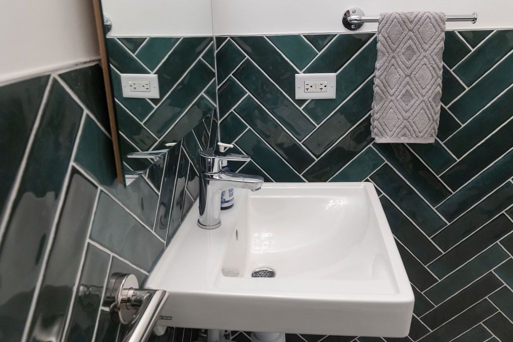White sink with chrome faucet against green herringbone tile. Towel on rack.