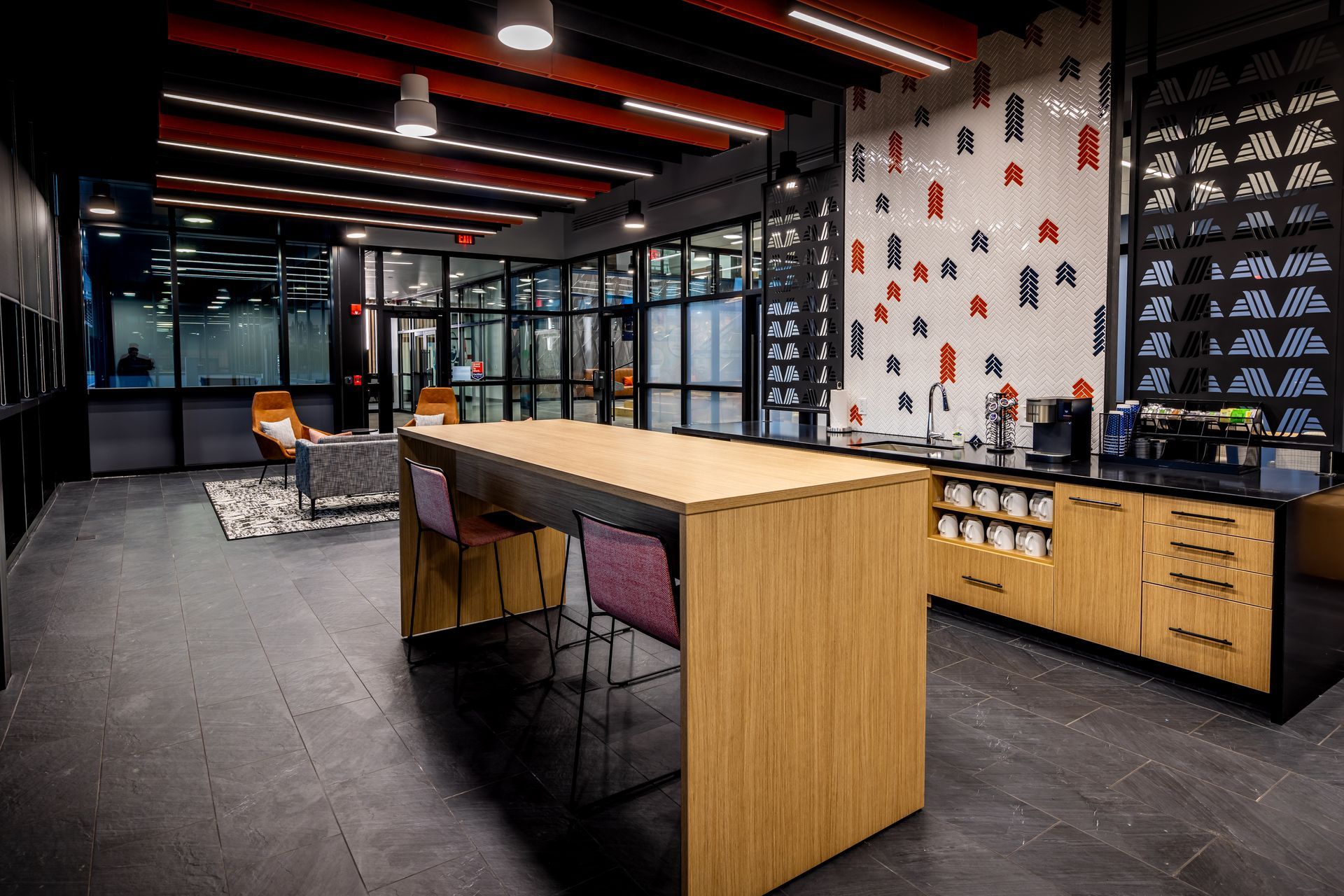 Modern office breakroom with a large wooden table and chairs, coffee bar, and seating area with glass walls.