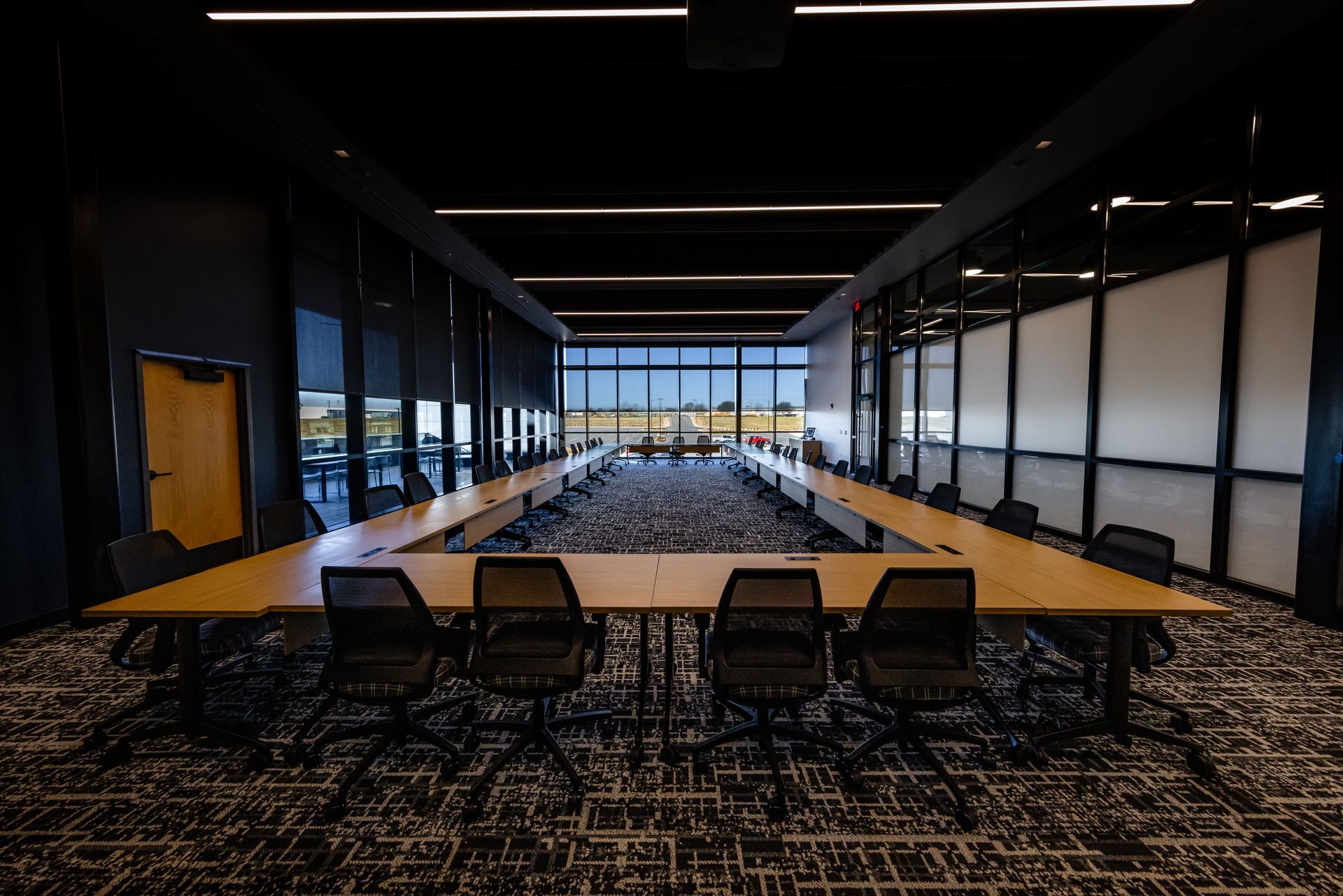 Conference room with U-shaped table, black chairs, and large windows with an outdoor view.