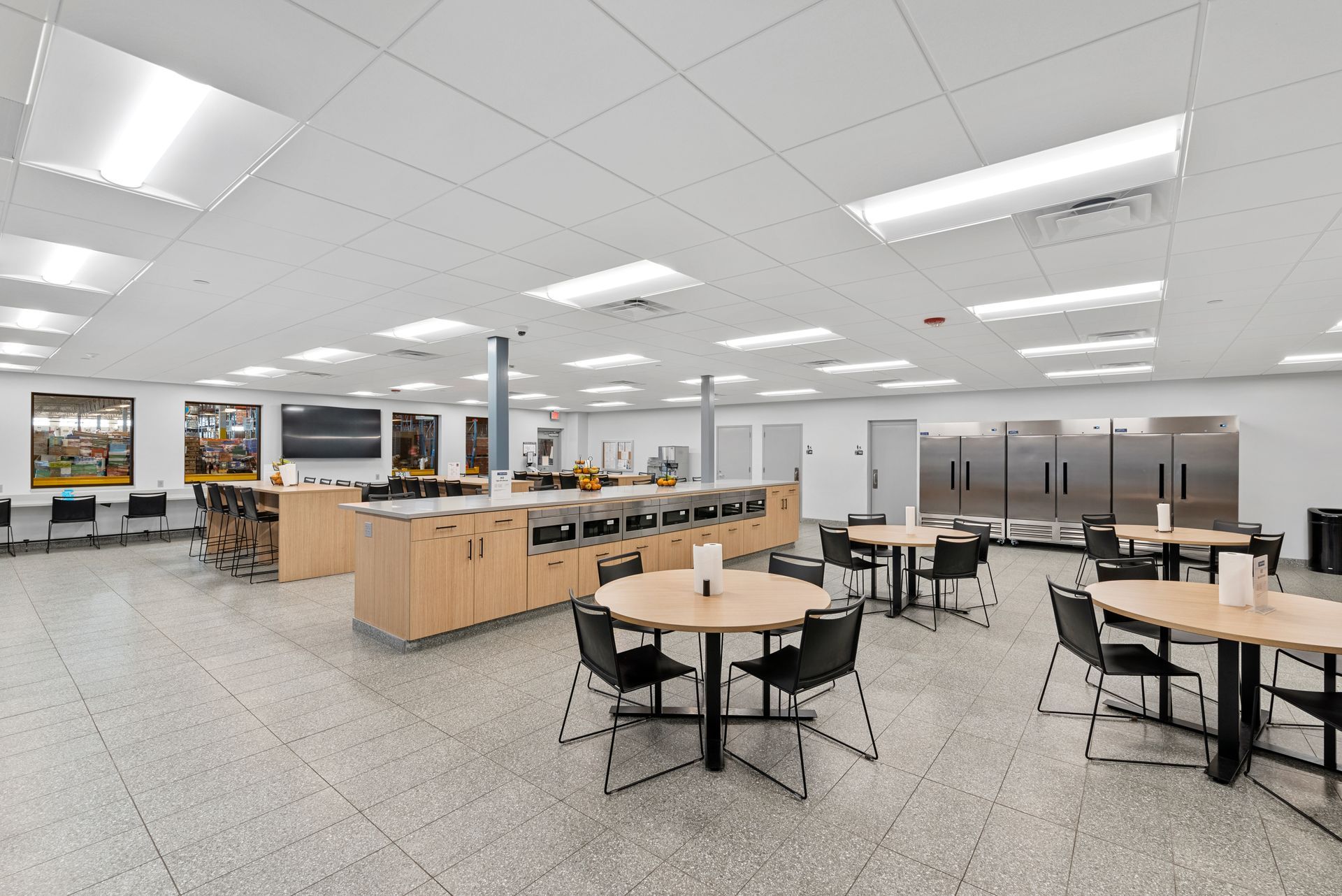 Brightly lit commercial kitchen with stainless steel appliances, tables, and workstations.