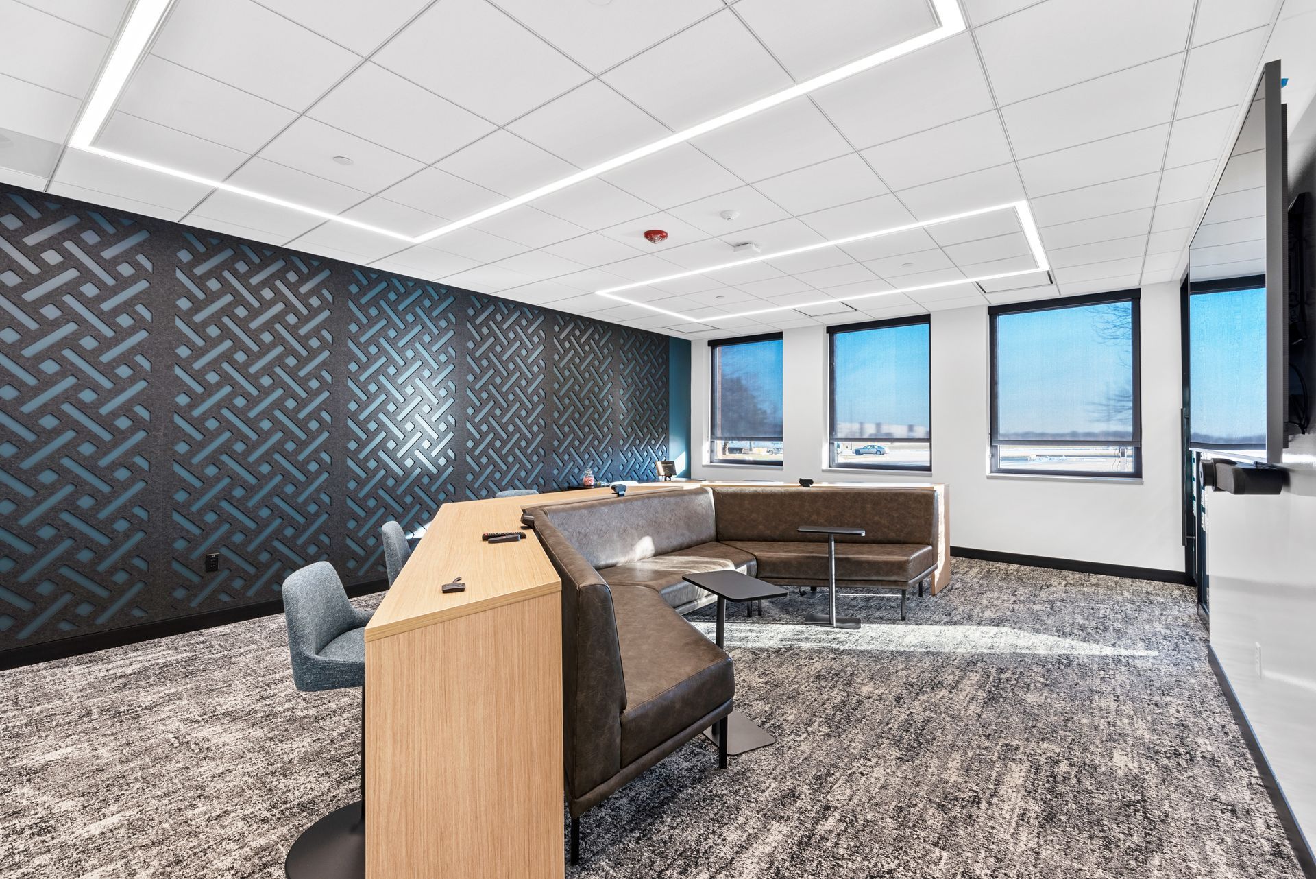 Modern lounge area with patterned wall, seating, large windows, and a TV.