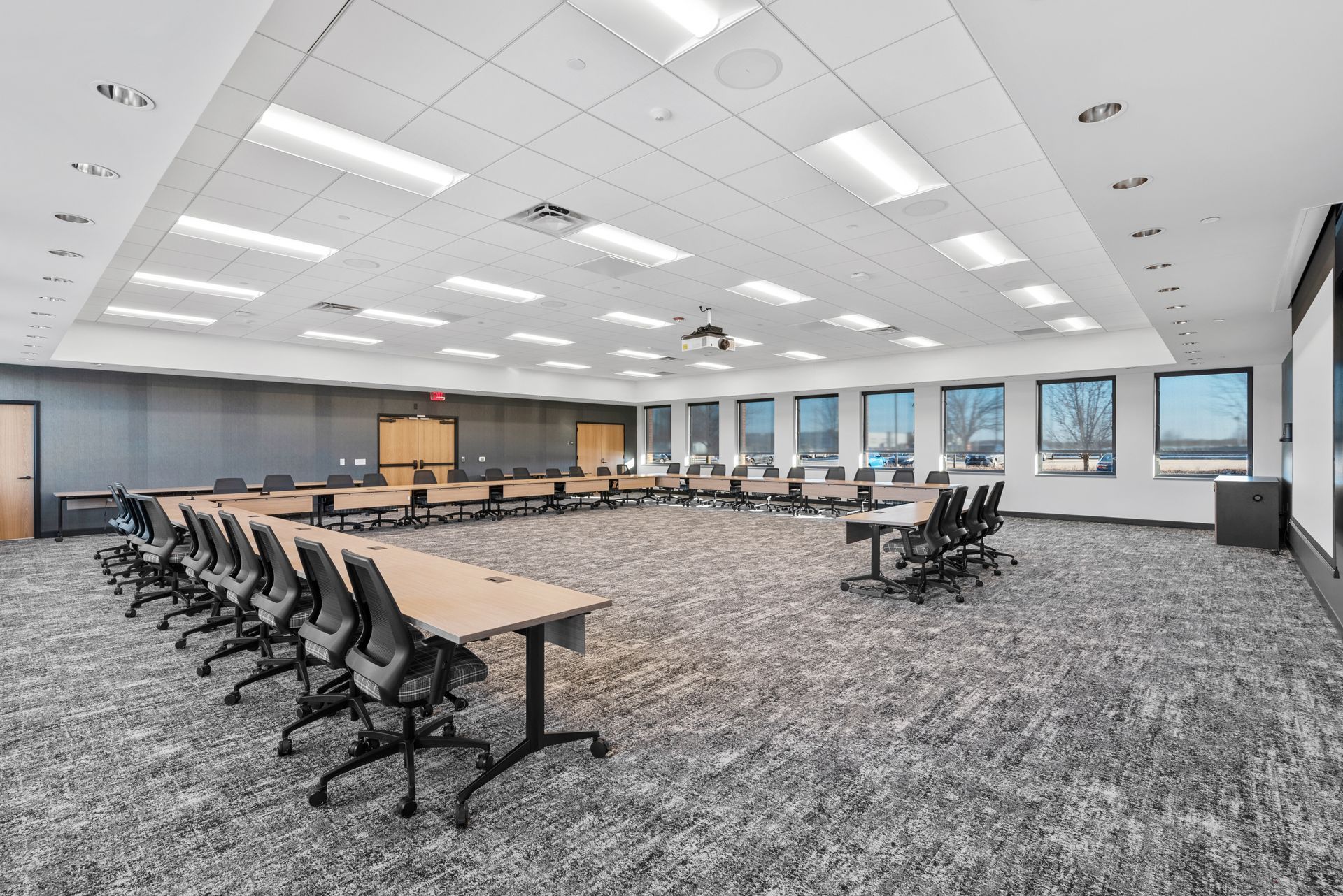 Conference room with tables arranged in a U-shape, black chairs, and windows.