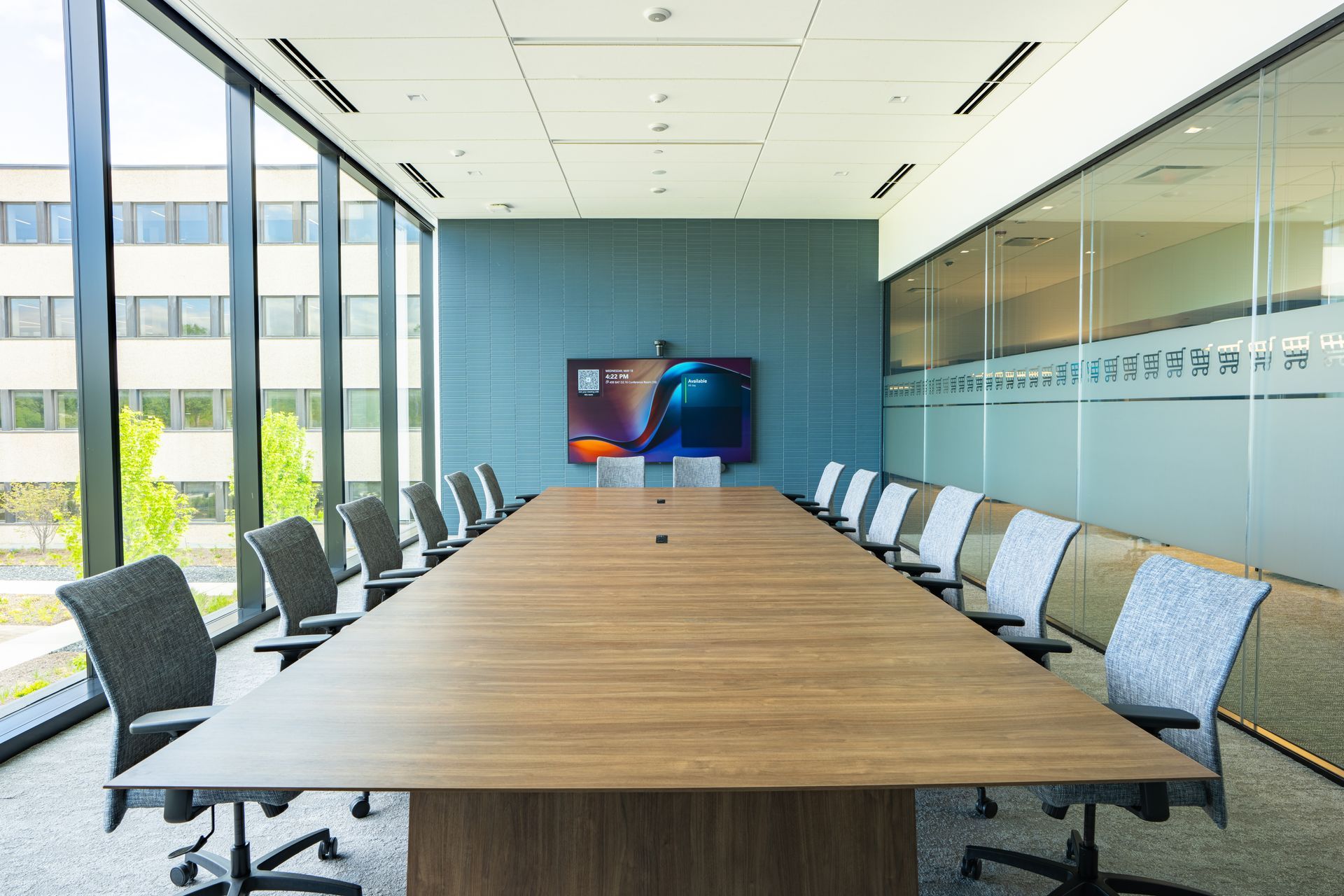 Conference room with a rectangular table, several chairs, and a large screen on a blue wall.