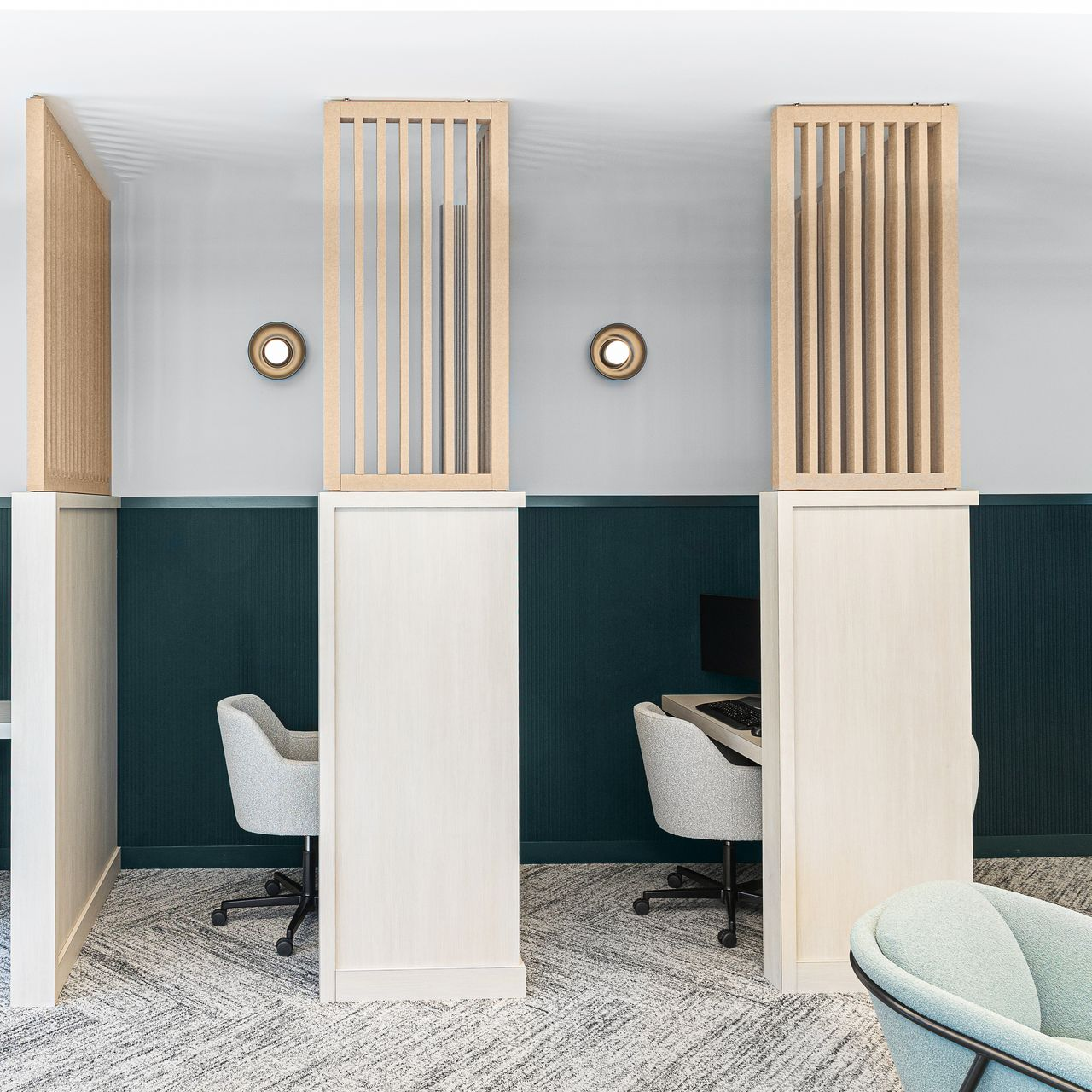 Office cubicles with desks and chairs, white and teal walls, light wood dividers, and sconces.