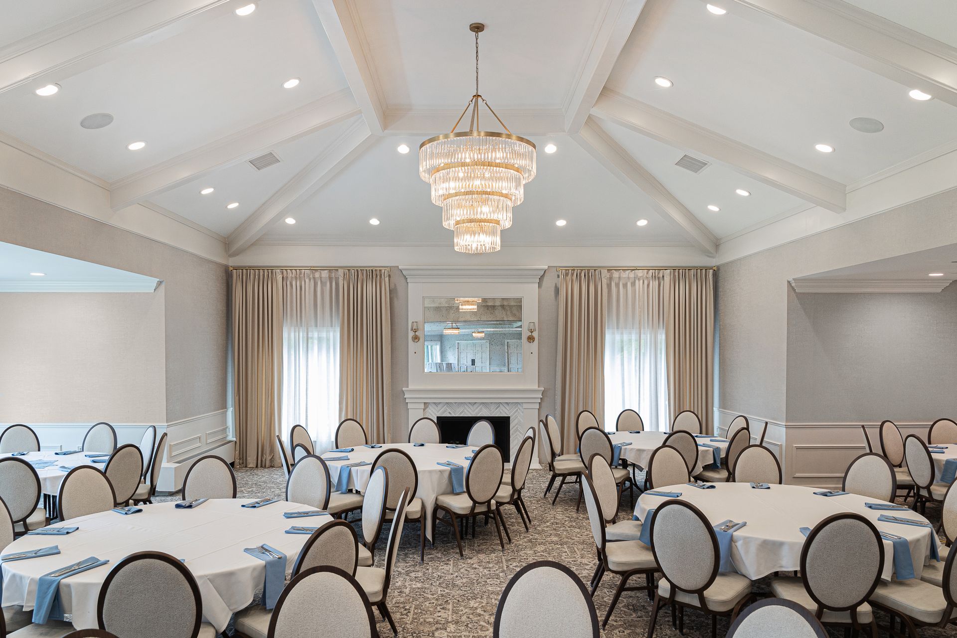 Elegant banquet hall with round tables set for a gathering, chandelier, fireplace, neutral colors.