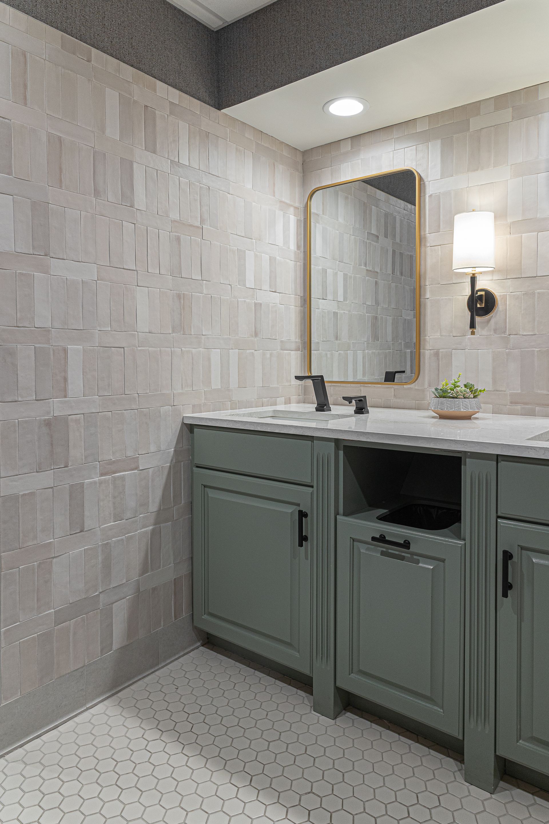 Bathroom with gray tile walls, sage green vanity, black fixtures, and a gold-framed mirror.