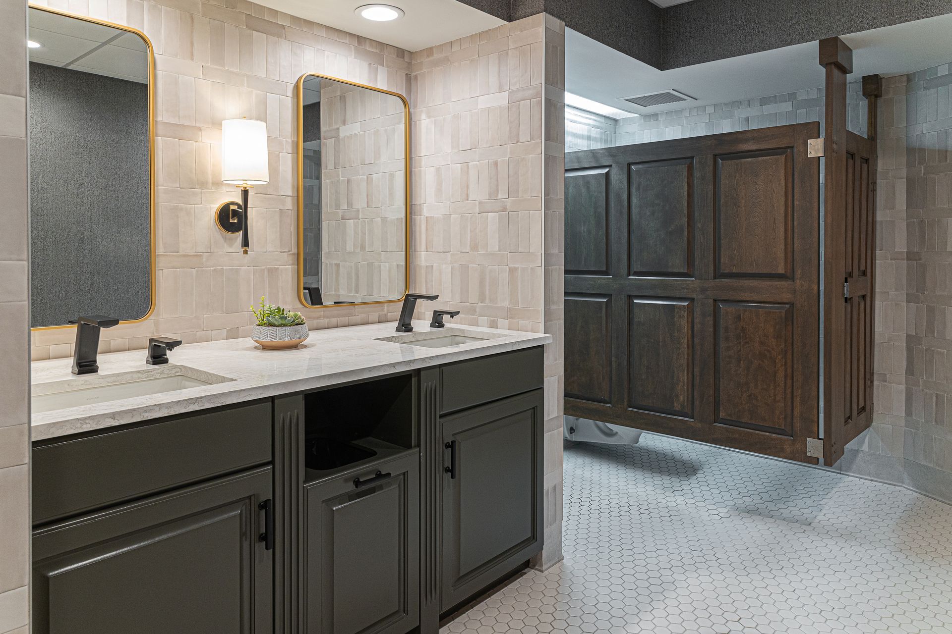 Modern public restroom with dark cabinets, two mirrors, and wood stall doors.