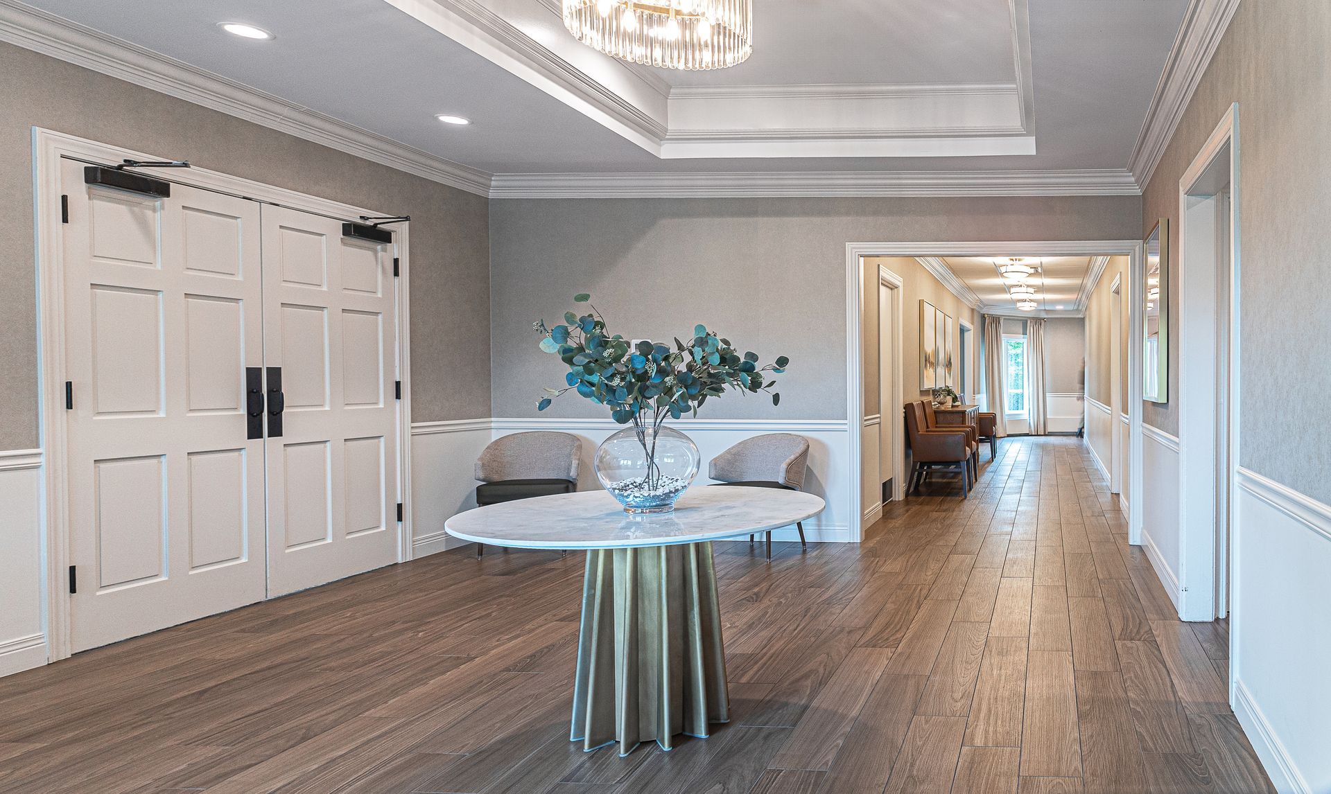 Elegant hallway with wood floors, white trim, and a marble-top table with a floral arrangement.
