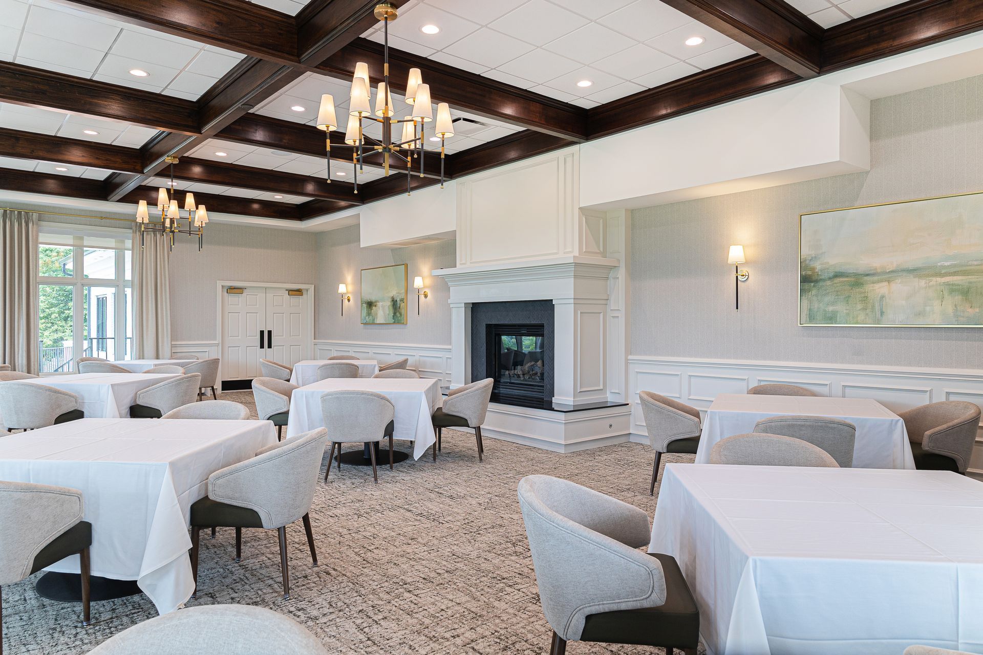 Elegant dining room with white tablecloths, chairs, fireplace, and chandeliers.