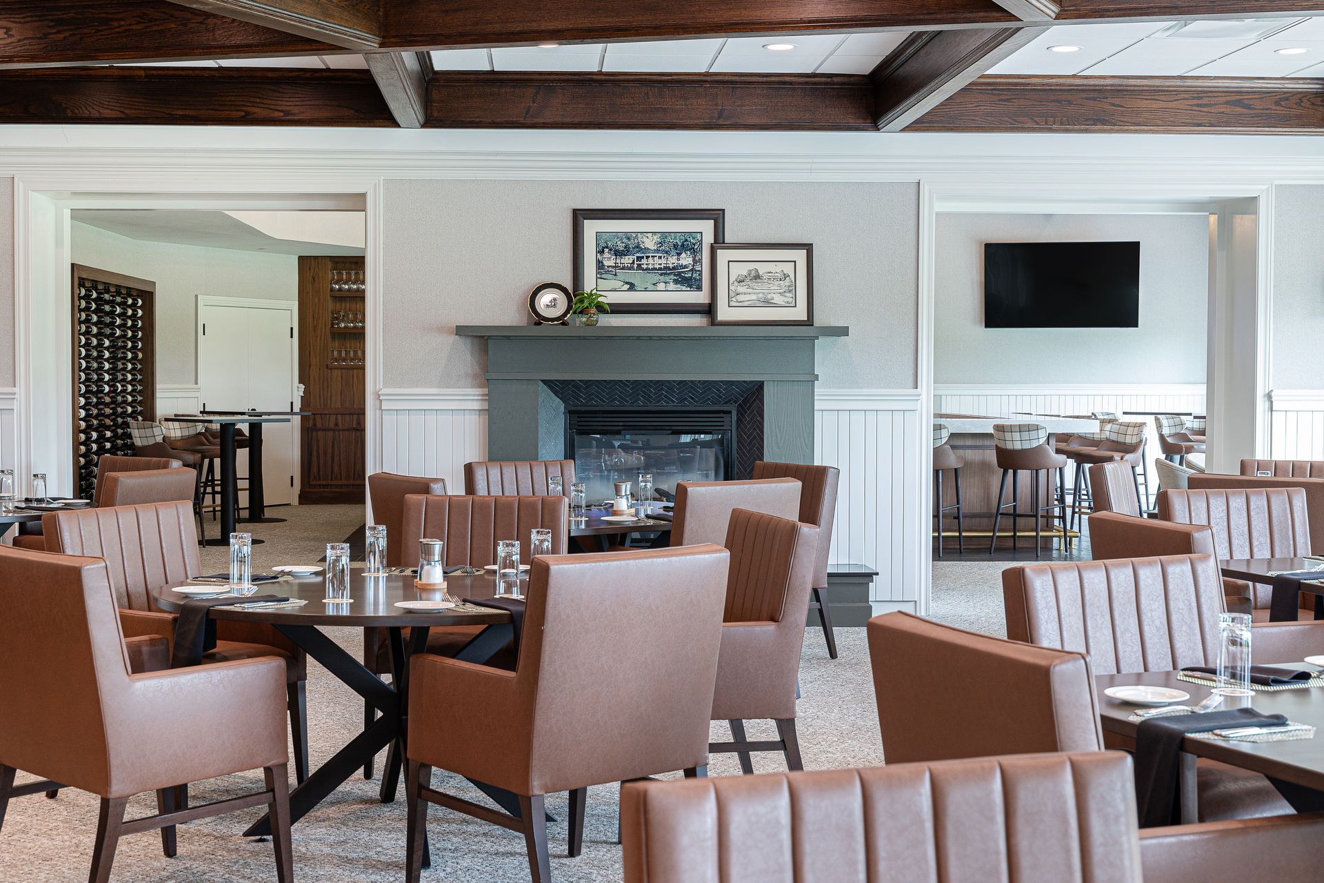 Restaurant interior with brown leather chairs, tables, fireplace, and TV on wall.