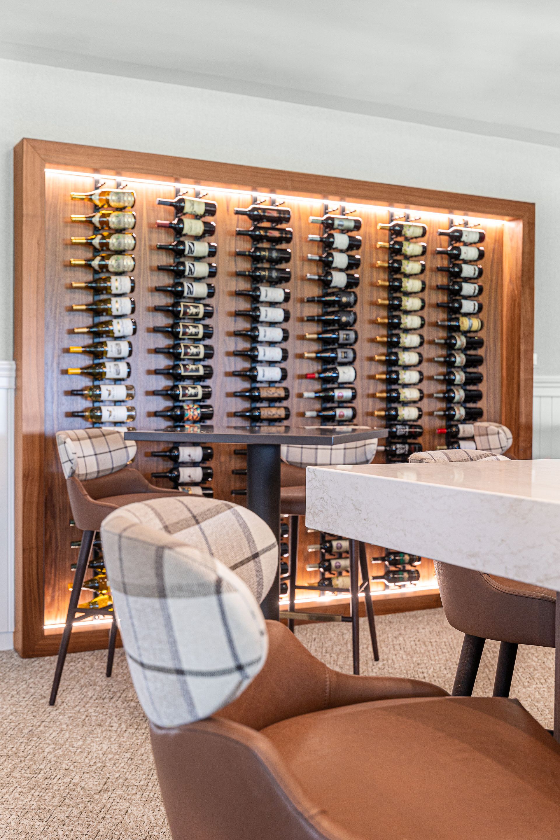 Wine rack with bottles, lit from behind, near a small table and chairs.