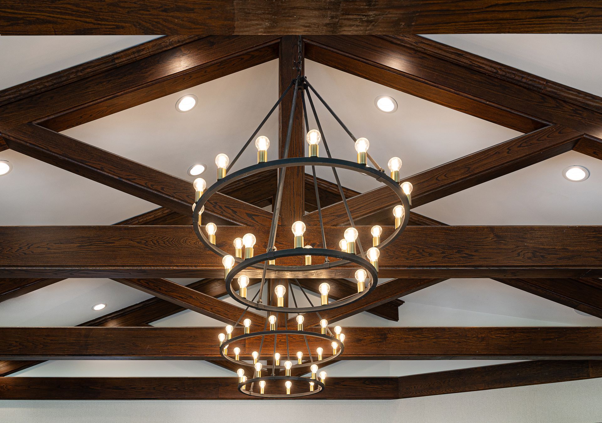 Dark wood beams on a white ceiling. A tiered, circular chandelier with many lights hangs.