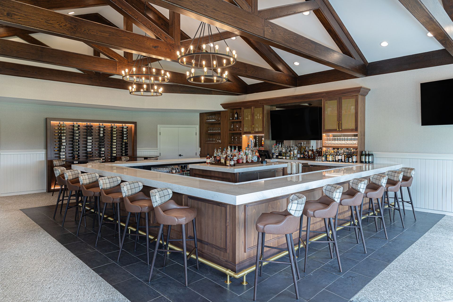Upscale bar with a large, square counter, seating, and overhead chandeliers.