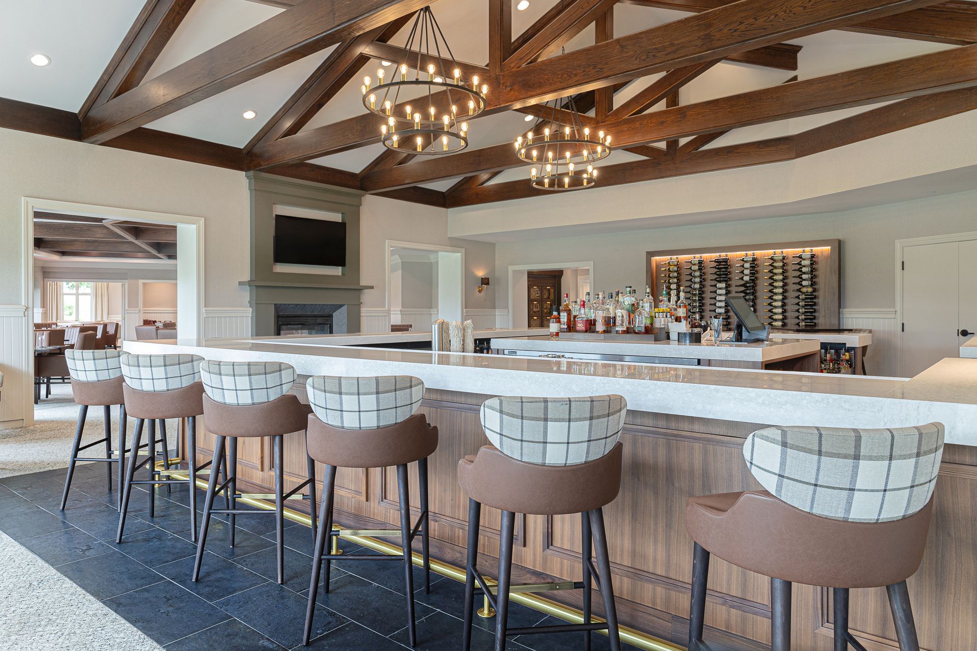 Bar with stools, overhead lighting, fireplace, wine rack, and exposed wooden beams.