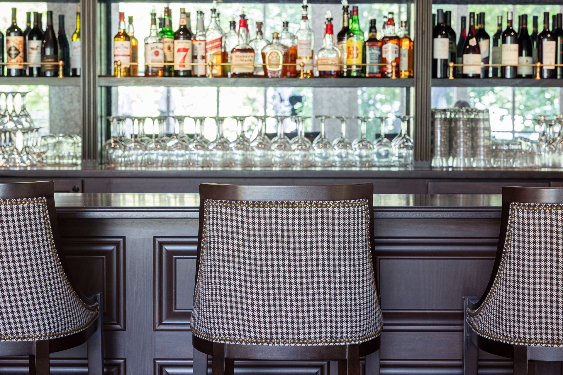 Bar stools with houndstooth seats face a bar stocked with liquor and glassware.