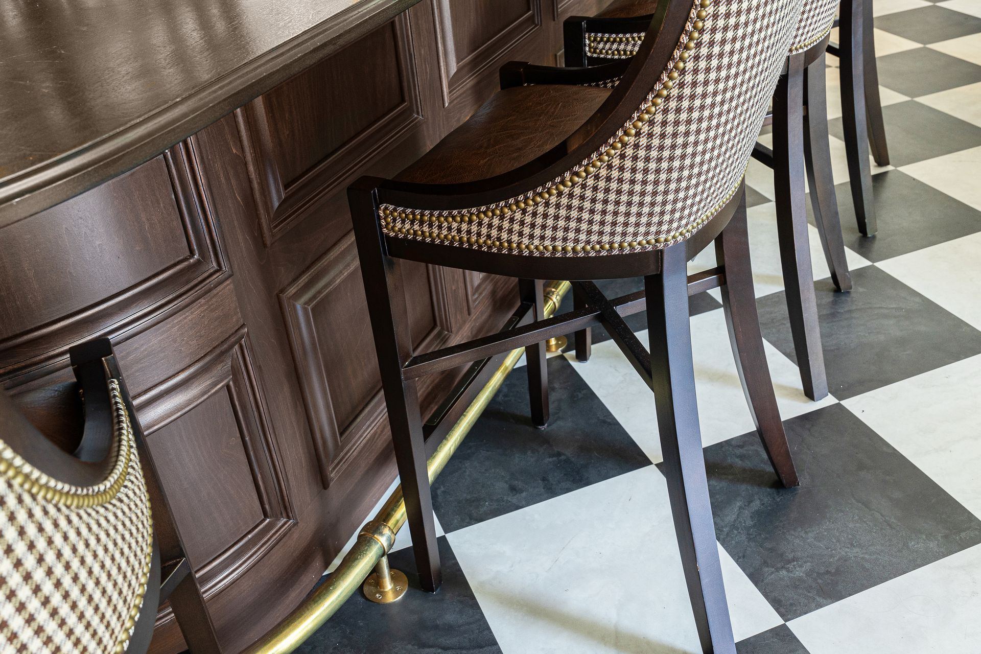 Bar stools with patterned seats at a dark wood bar. Black and white checkered floor.