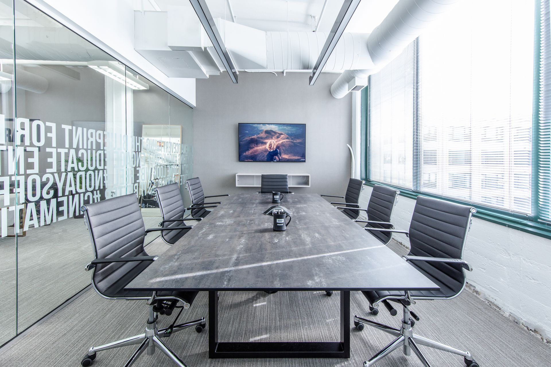 Modern office conference room with long table, chairs, TV, and large windows.