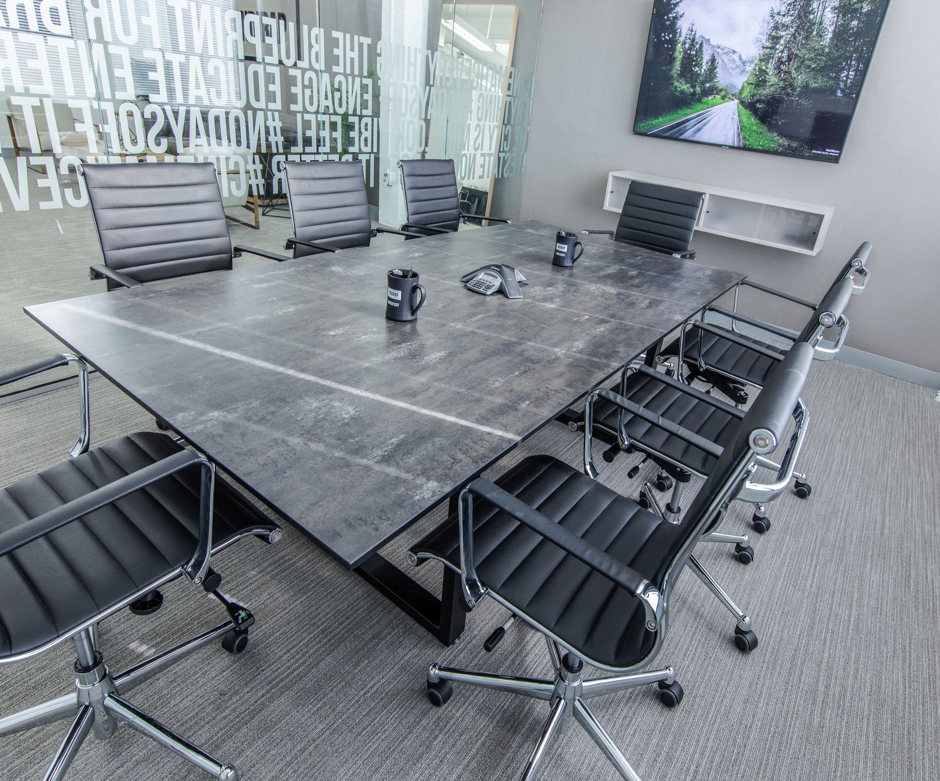 Conference room with large gray table, black chairs, and a TV.