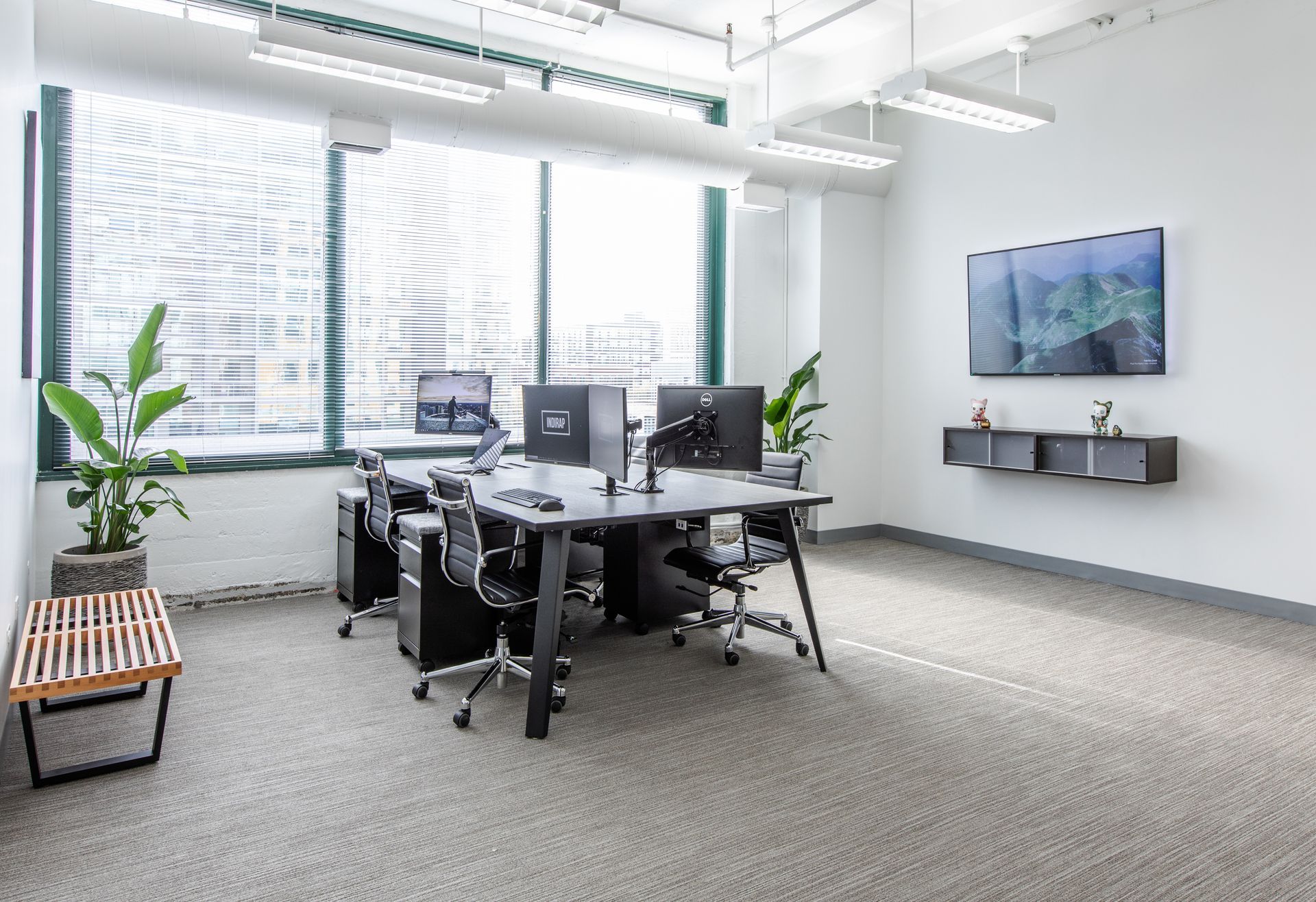 Modern office space with desks, computers, chairs, a television, and large windows.