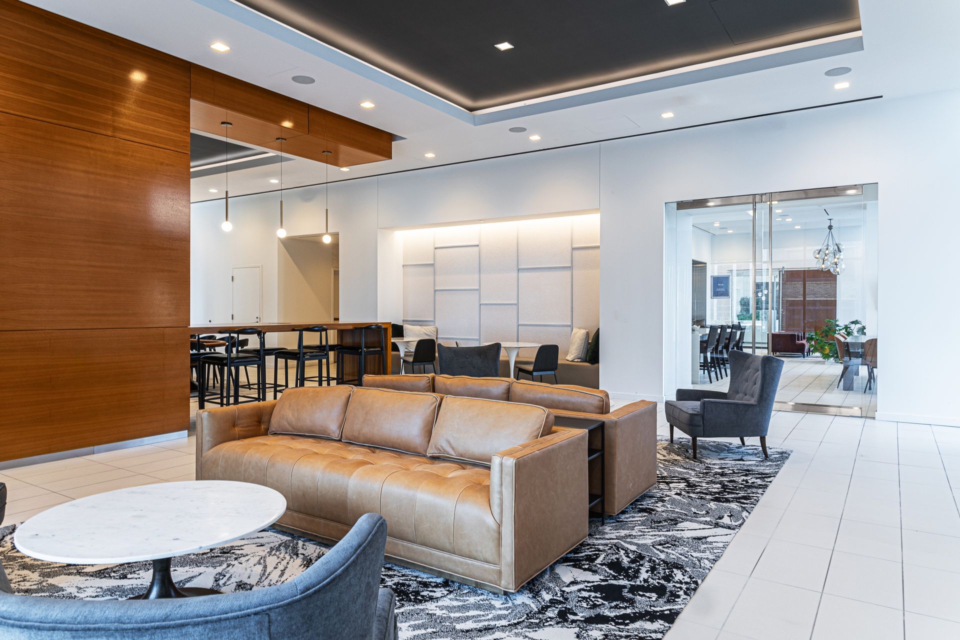 Modern lobby lounge with tan sofas, marble tables, and black chairs in a bright, open interior