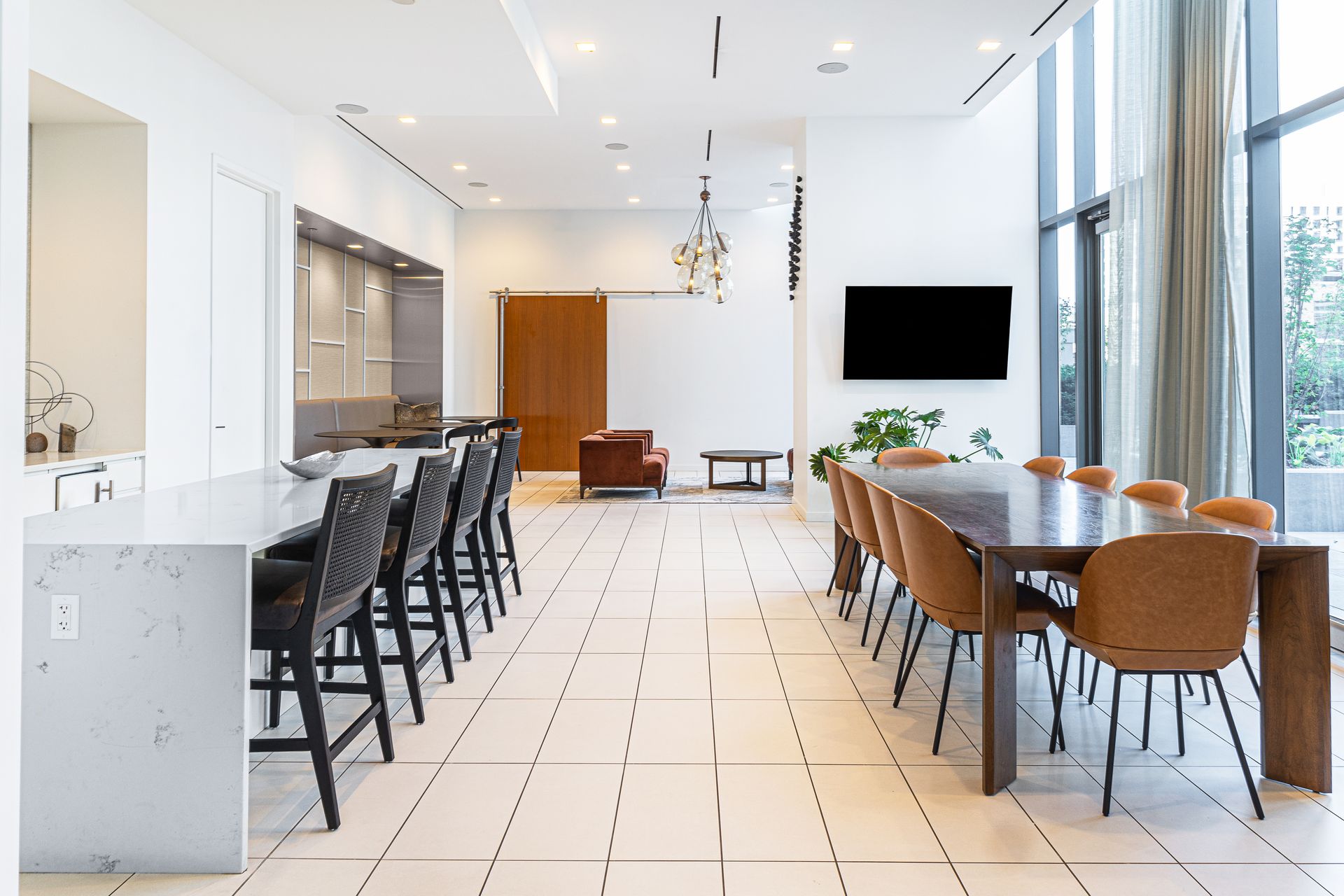 Modern, bright communal space with a large kitchen island, long dining table, seating, and a TV.