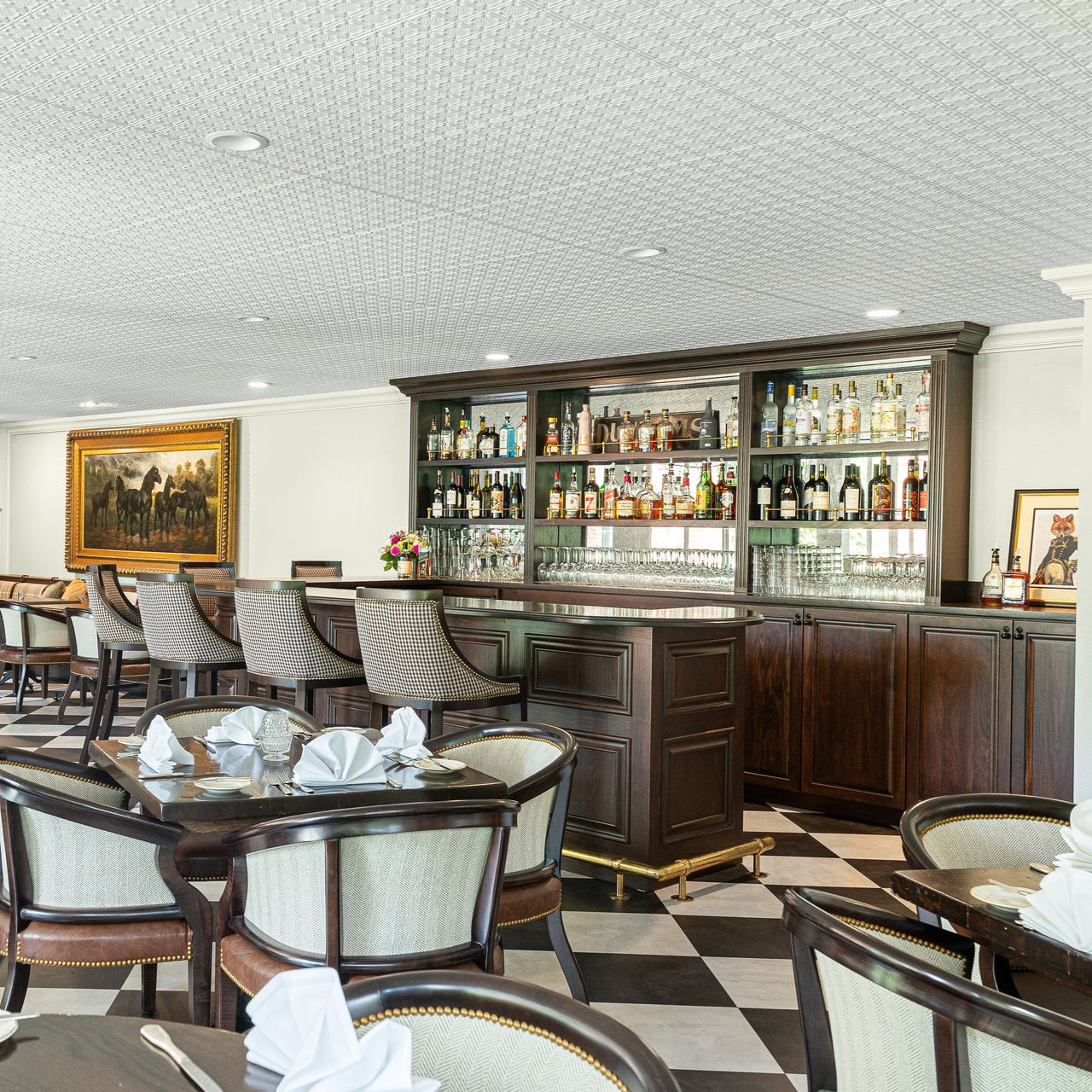 Restaurant interior with a bar and tables. Dark wood, black and white checkered floor, bottles on shelves.