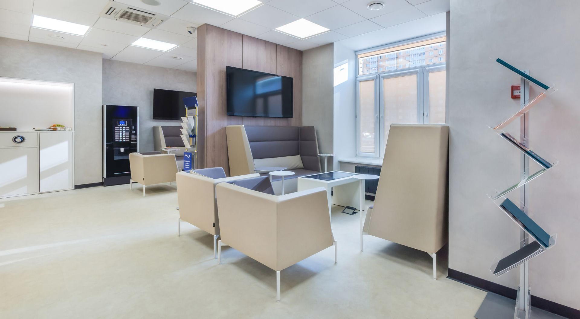 Modern office lounge with white chairs, wall-mounted TV, windows, and a blue zigzag floor lamp