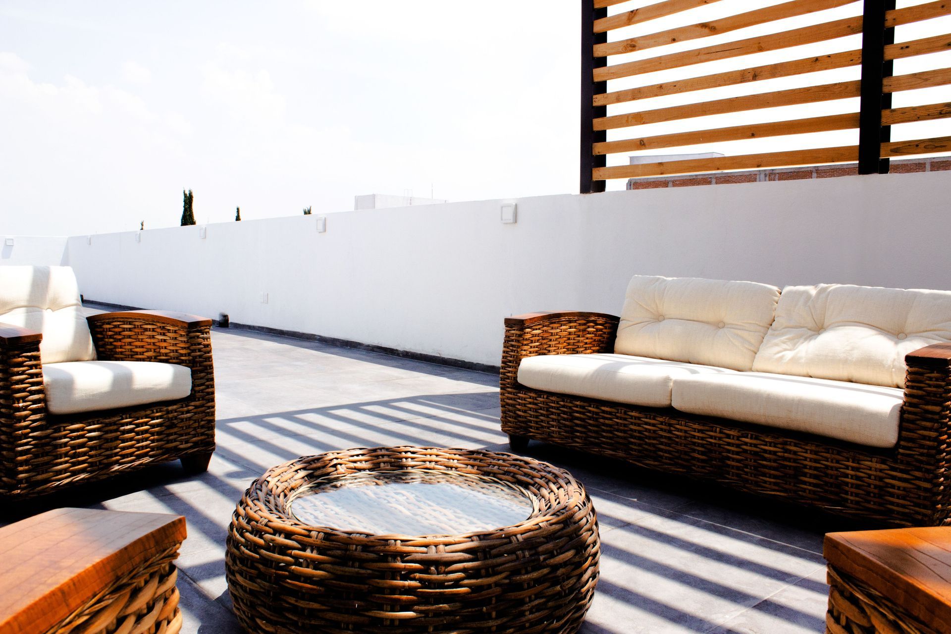 Outdoor patio with wicker furniture, cream cushions, and striped shadows under a bright sky