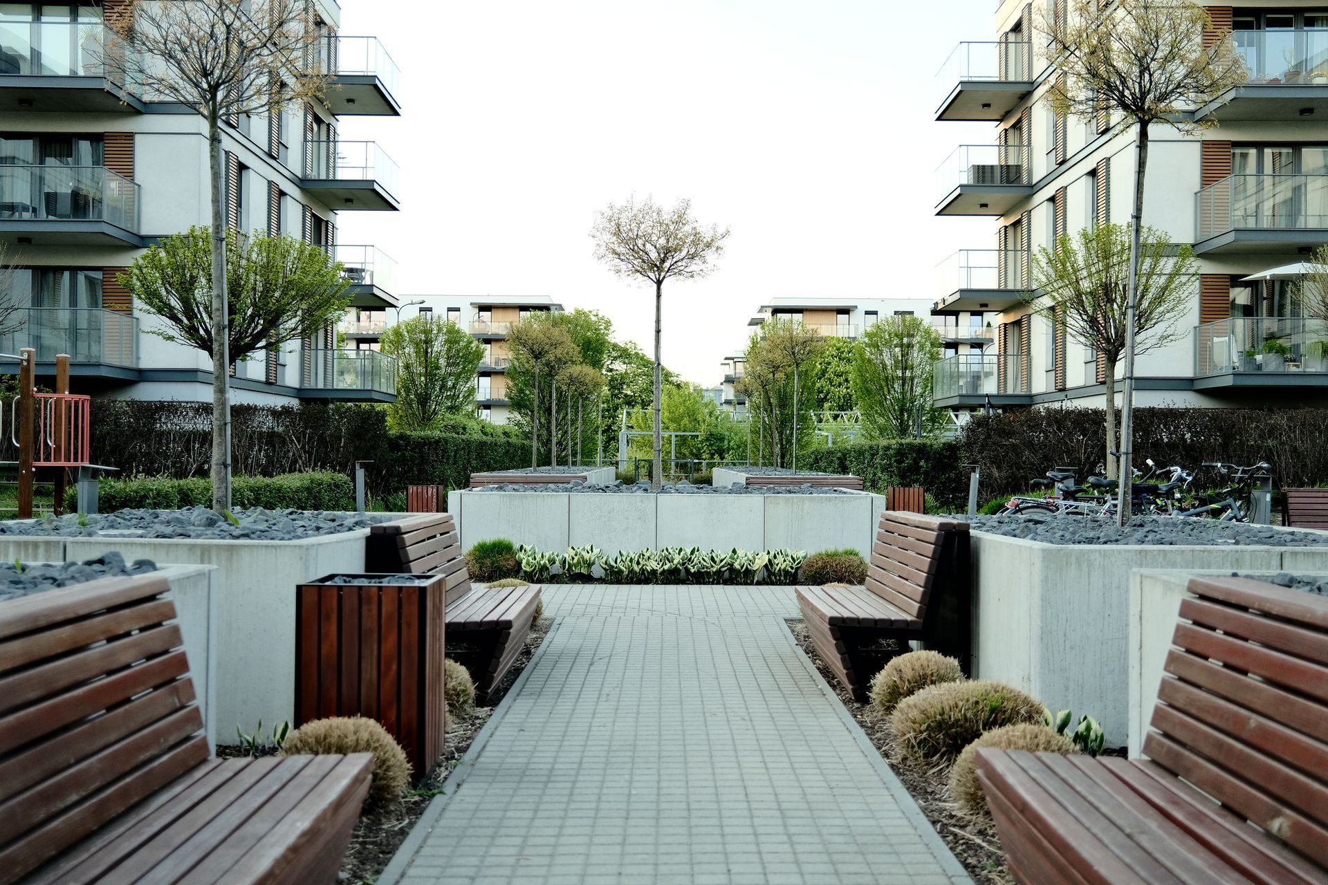 Modern apartment courtyard with benches, paved path, planters, and trees between two buildings