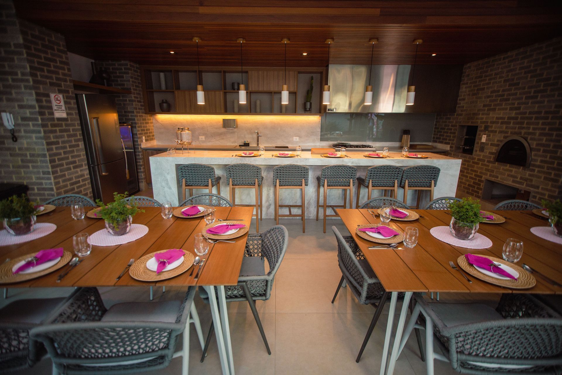 Rustic dining room with set tables, pink placemats, brick walls, and a bar counter in the background