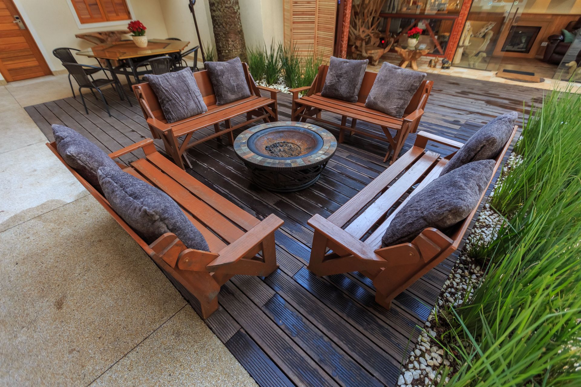 Outdoor patio seating area with wooden chairs around a round fire pit, beside a doorway and plants