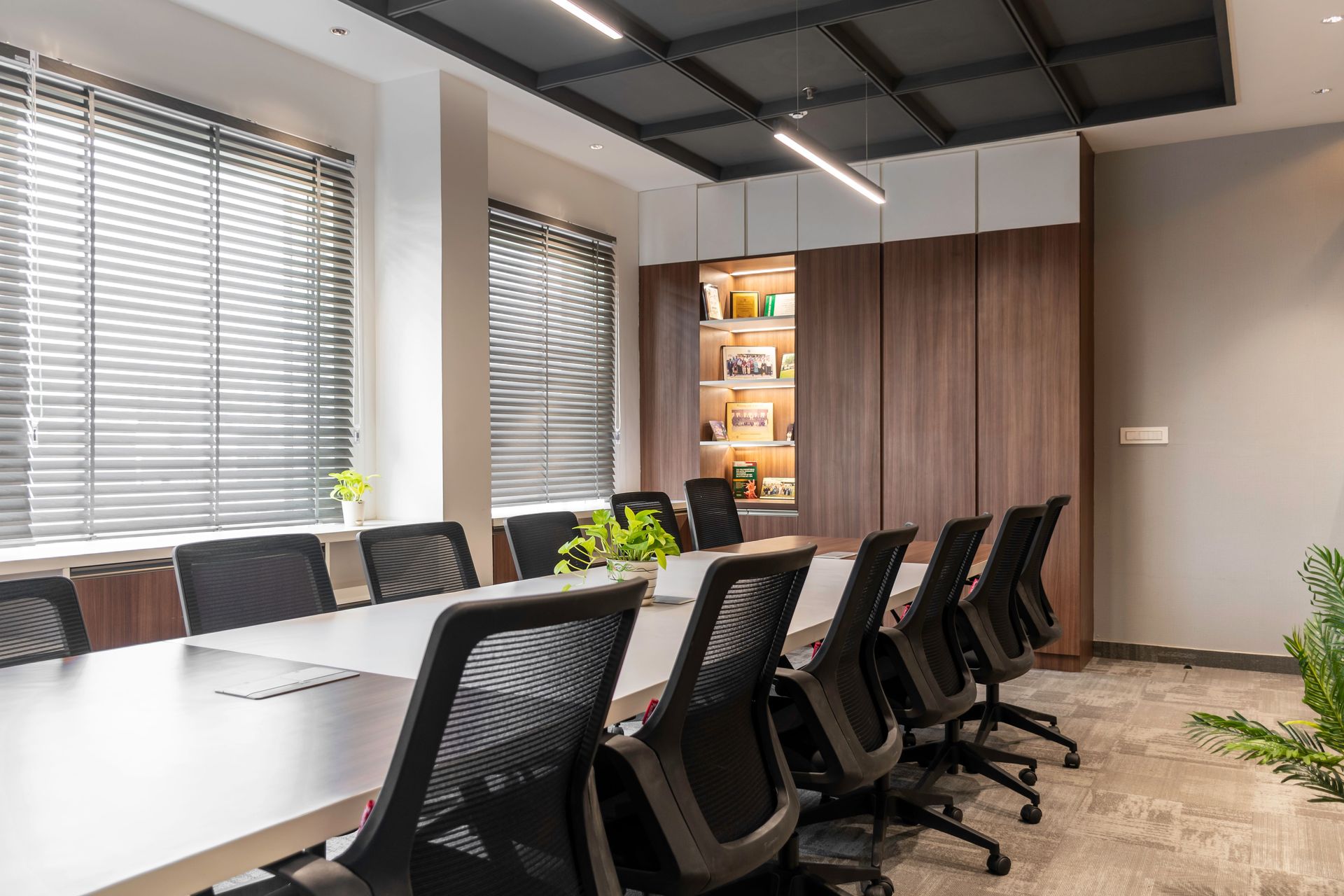 Modern conference room with long white table, black office chairs, large windows, and wood cabinets