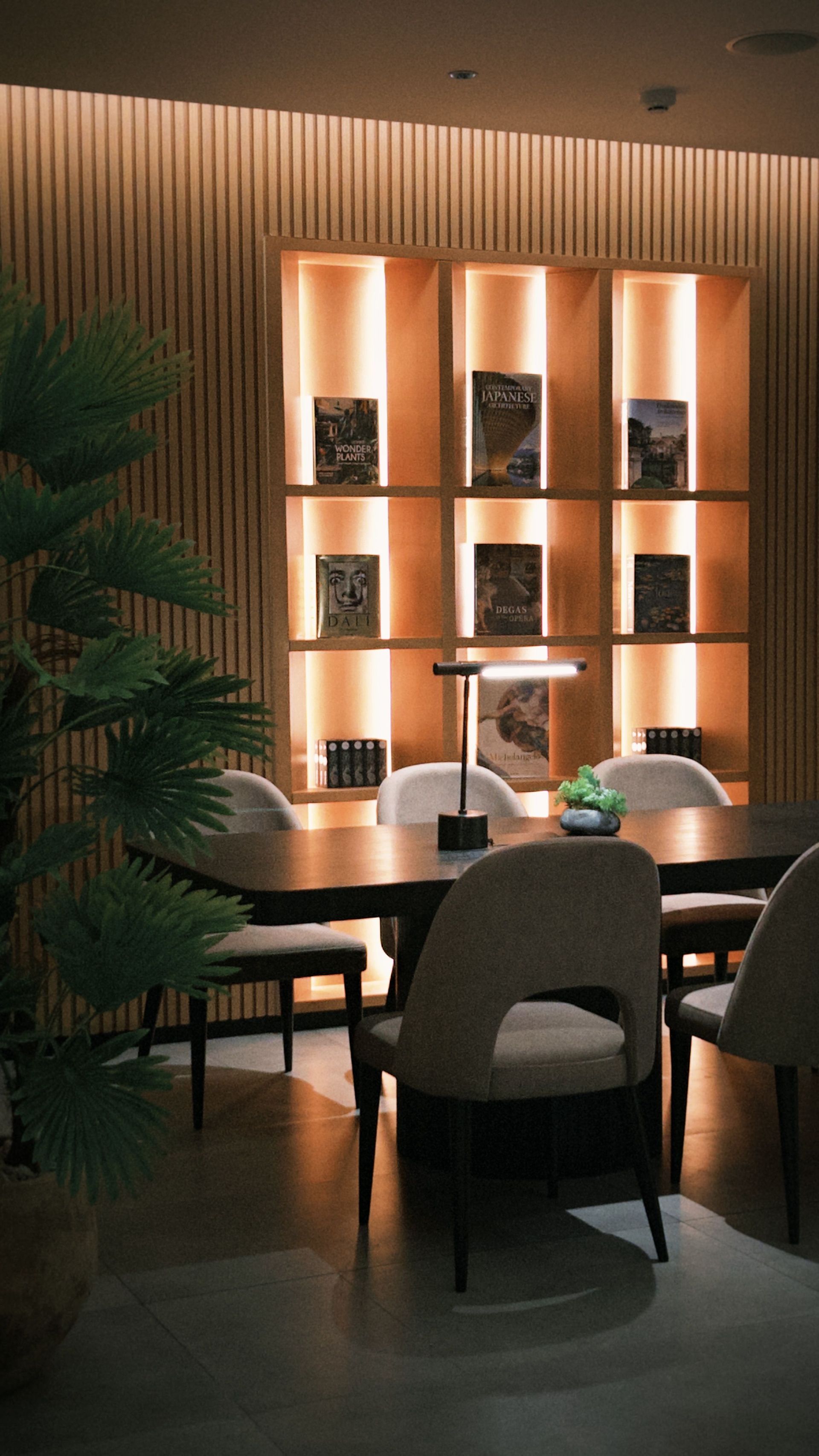 Cozy modern dining area with upholstered chairs, small tables, and backlit shelving against a wood wall.