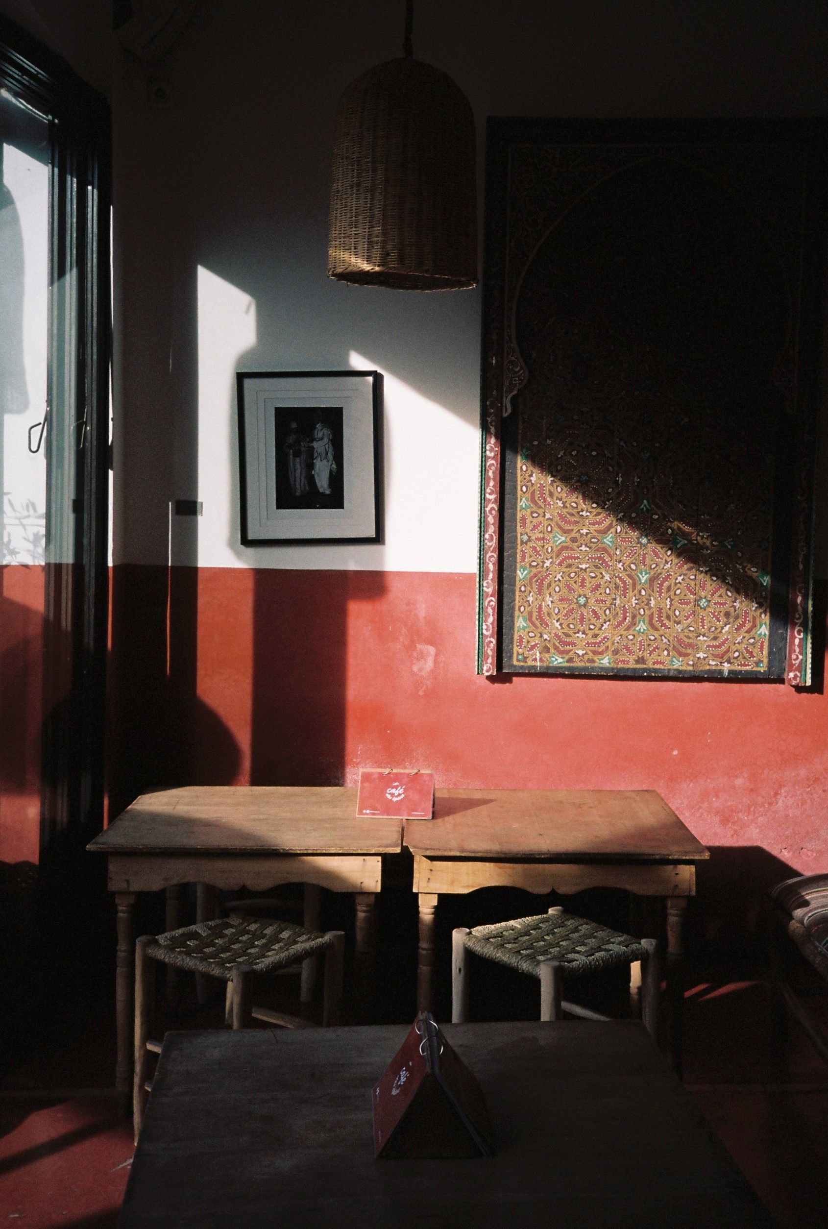 Small café corner with two wooden tables and chairs beside a sunlit red-and-white wall.