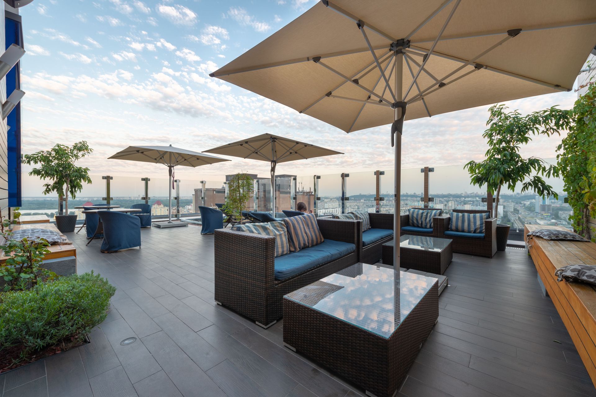 Rooftop lounge with wicker seating, beige umbrellas, and ocean view at sunset