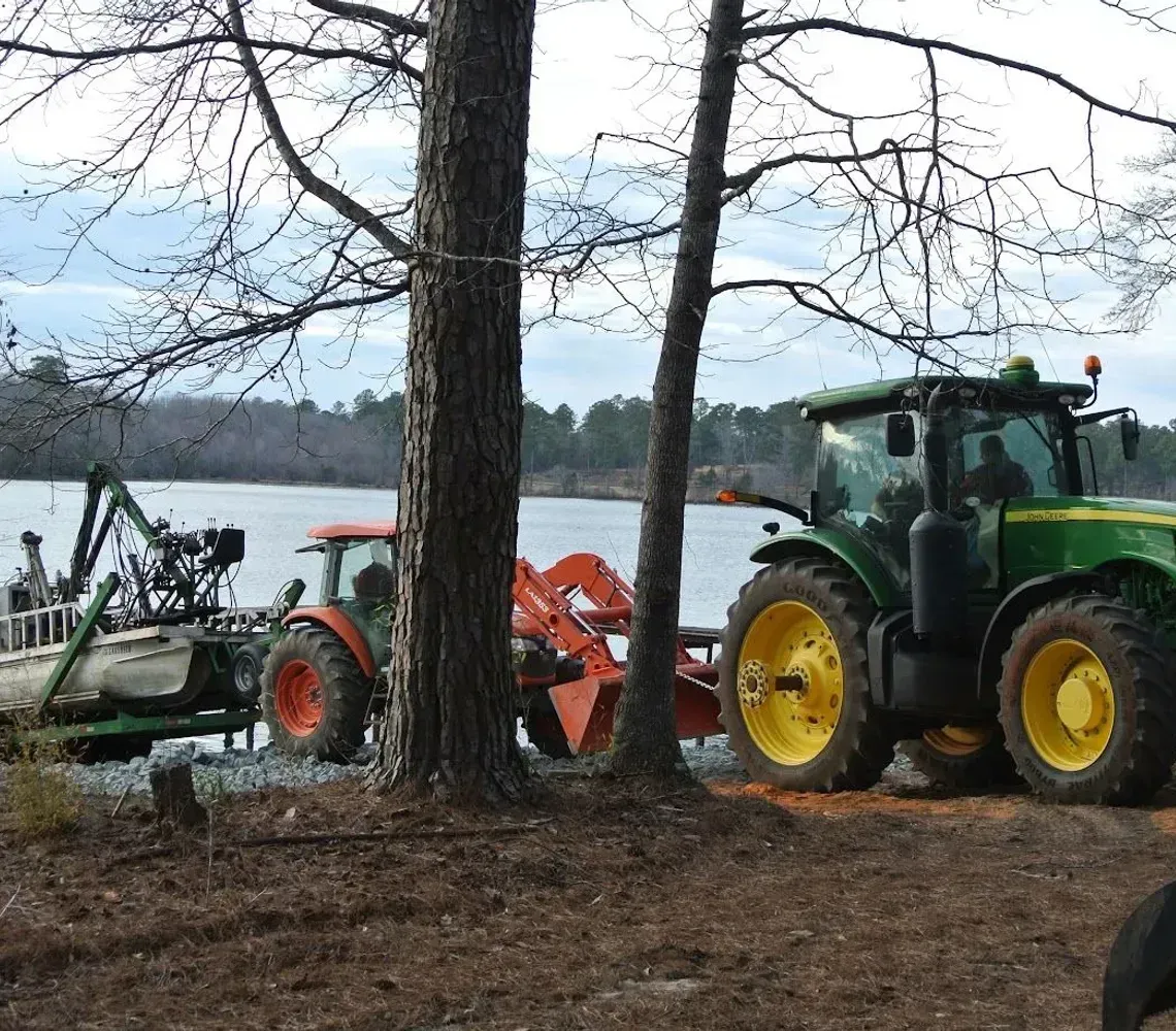 Yellow backhoe loader digging soil in a muddy field under a clear sky