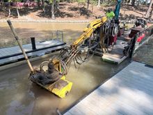 Yellow workboat with equipment on blue water near a tree-lined shoreline