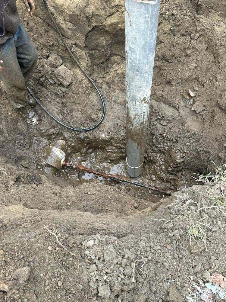A man is working on a pipe in the dirt.