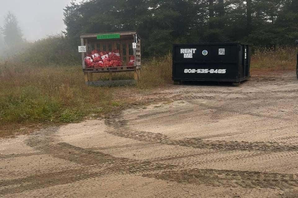 A dumpster is sitting in the middle of a dirt field.