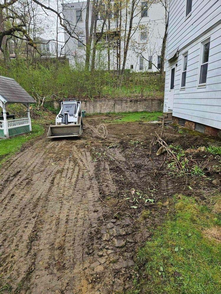 A bulldozer is driving down a dirt road in front of a house.