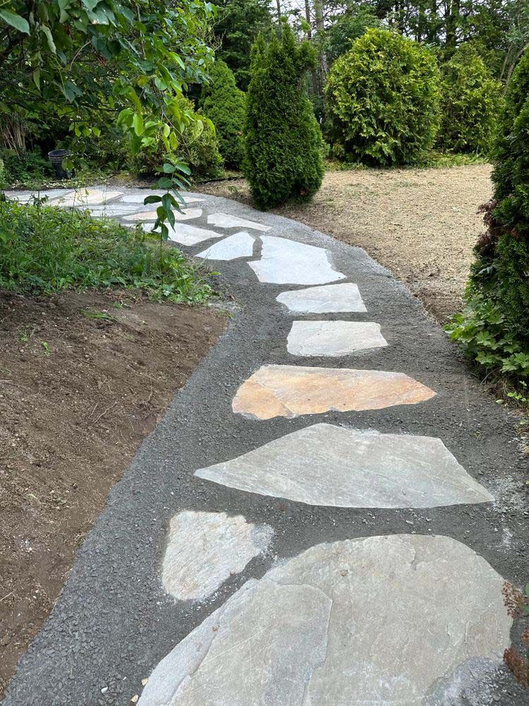 A stone walkway in a garden surrounded by trees and bushes.